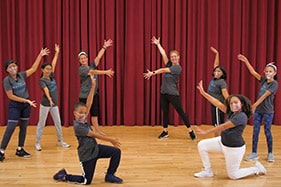 Two teaching artists and six student dancers stand in pose with outstretched arms
