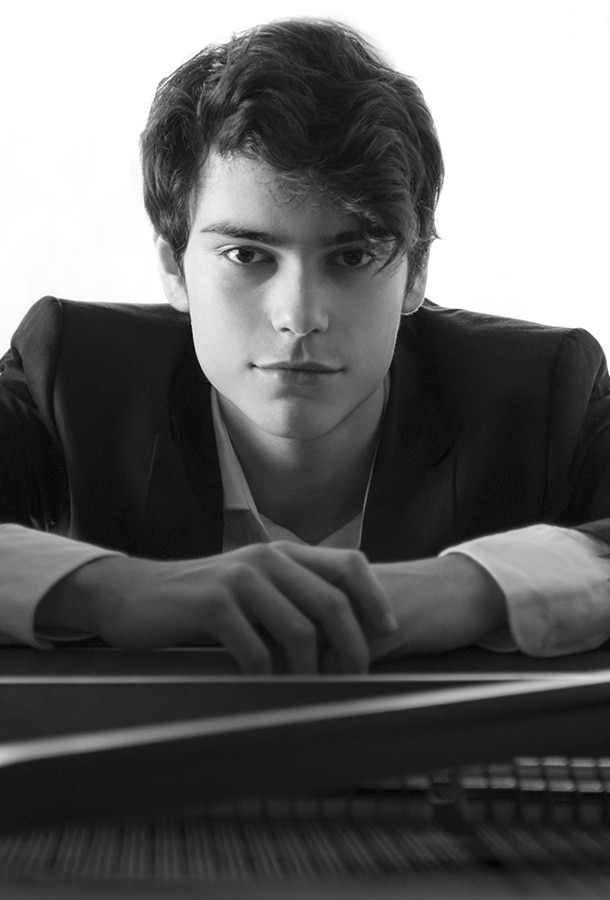 Tom Borrow poses in black and white at his piano, looking right into the camera.
