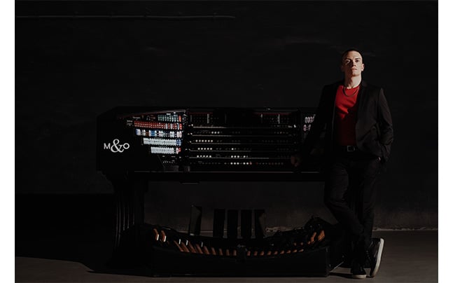 Image of Cameron Standing in front of full Digital Organ displaying its many stops, keys, and pedals.