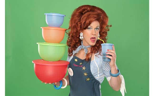 Dixie in an apron holding stacked turperware and drinking from a glass