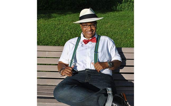 Dr. TreaAndrea Russworm sitting on a bench in suspenders, bowtie, and hat