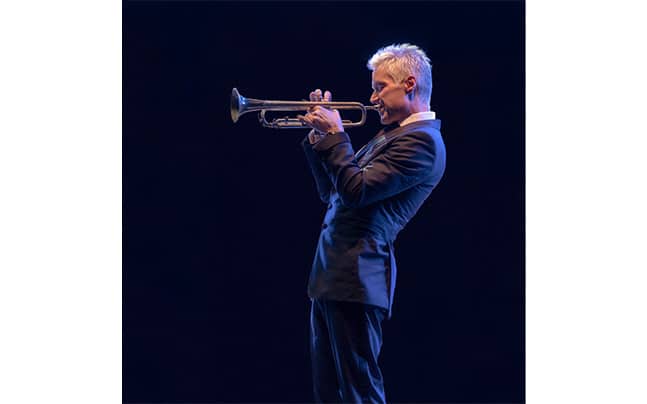 Chris Botti playing trumpet, facing left, black background