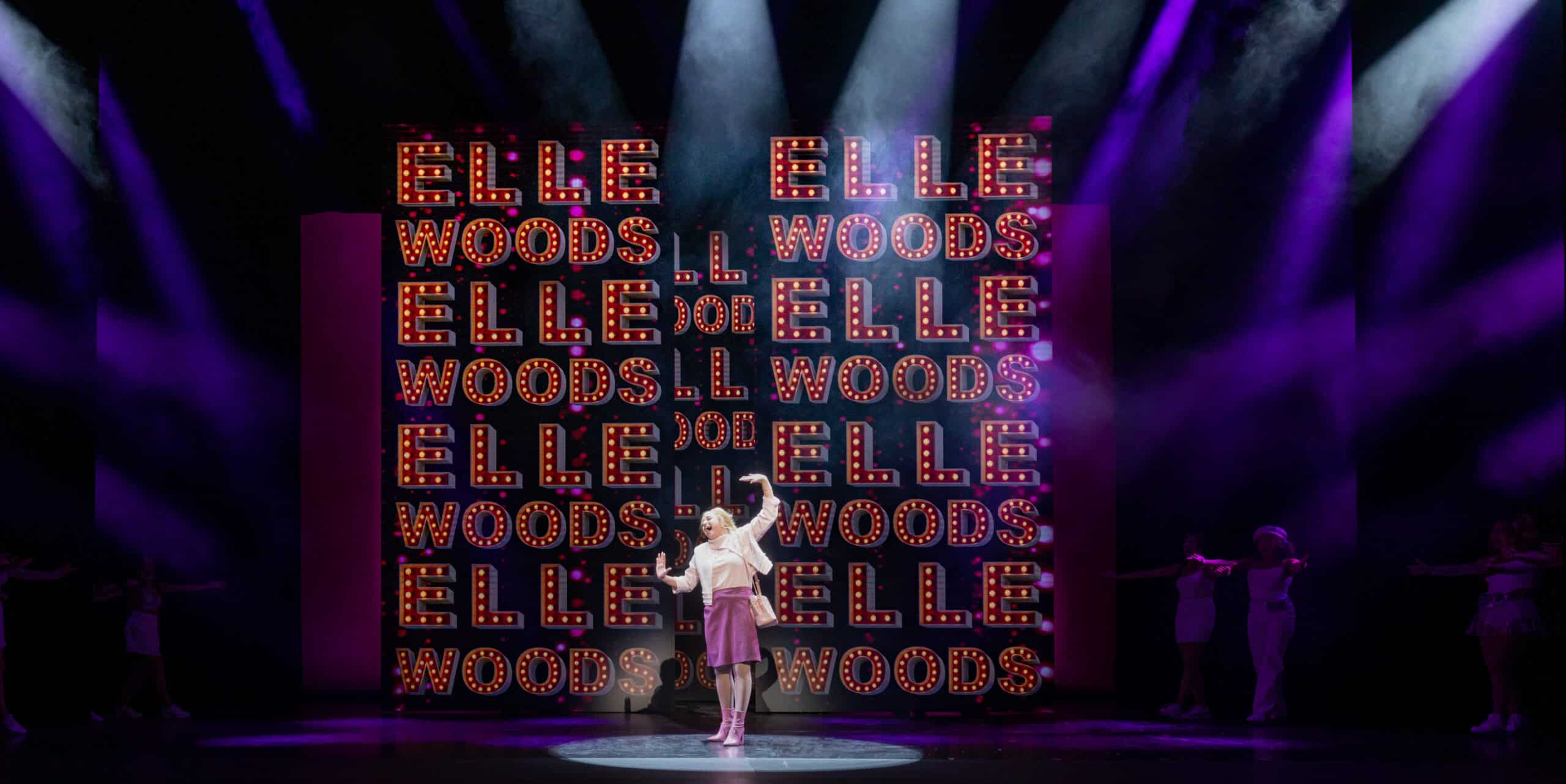 Elle Woods standing center stage with her name in lights behind her.