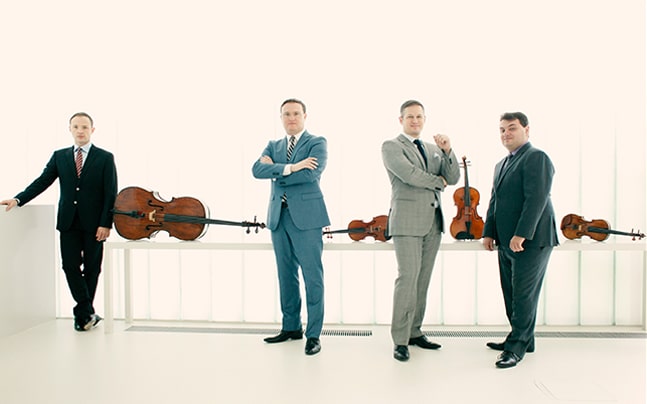 Quartet wearing blue suits with instruments on counter behind them.