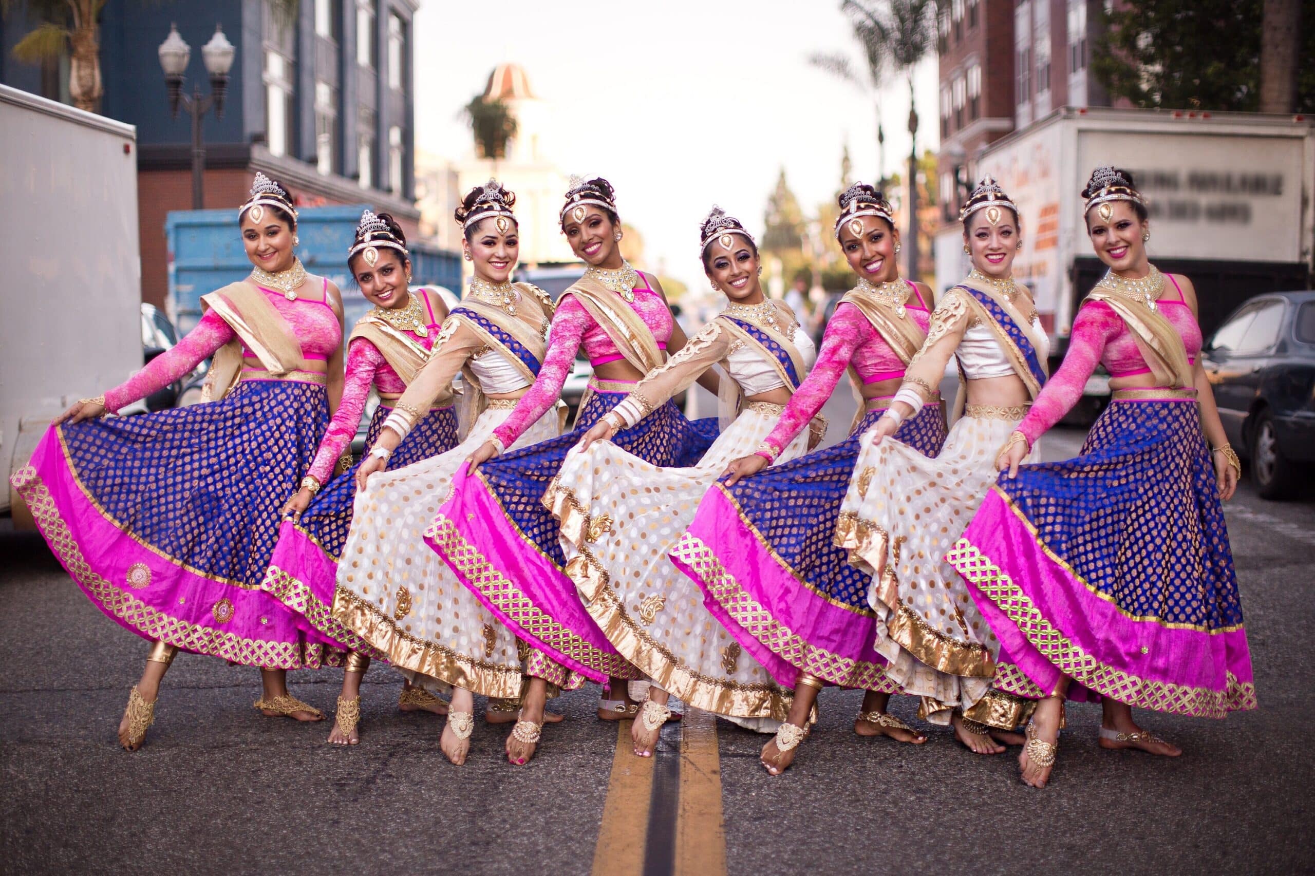 8 members of Rhythm India standing in street holding purple and pink skirts out.