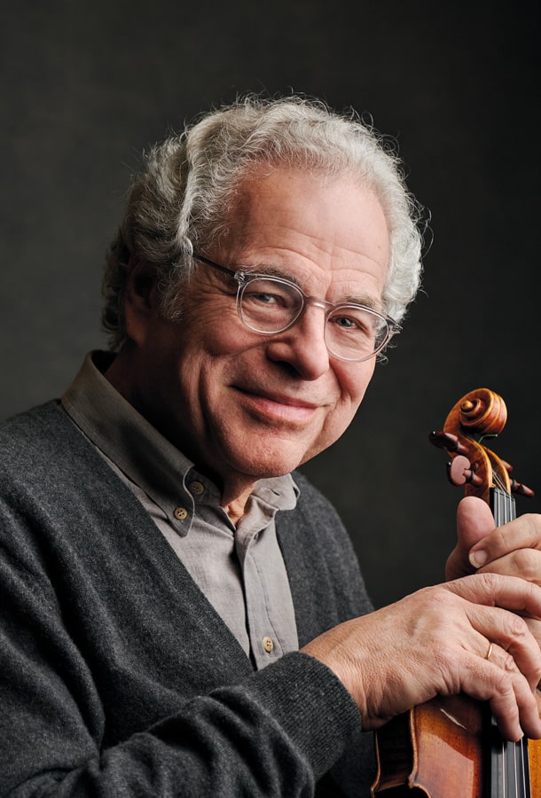 Itzhak Perlman smiling into camera holding neck of violin.