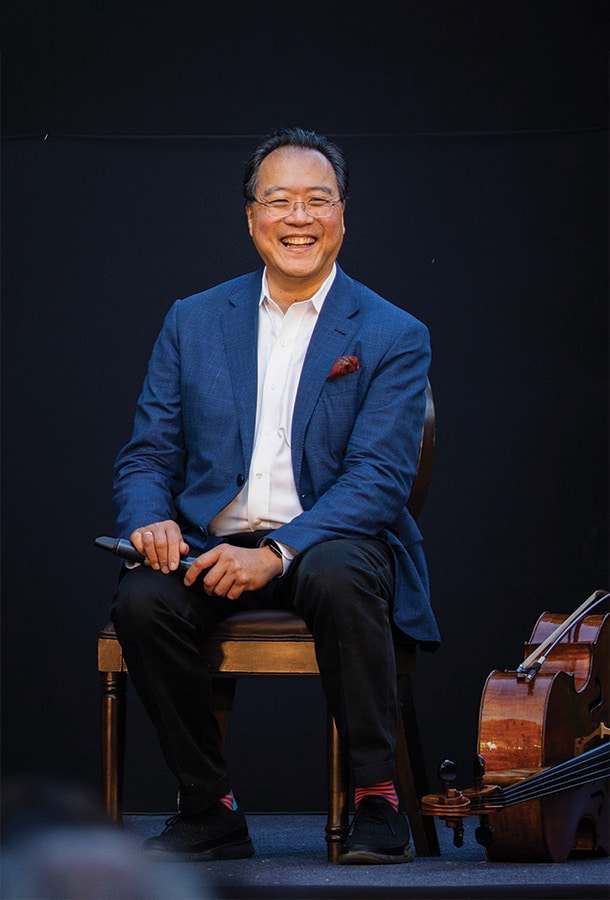 Yo-Yo Ma Sitting next to cello, holding a microphone, smiling