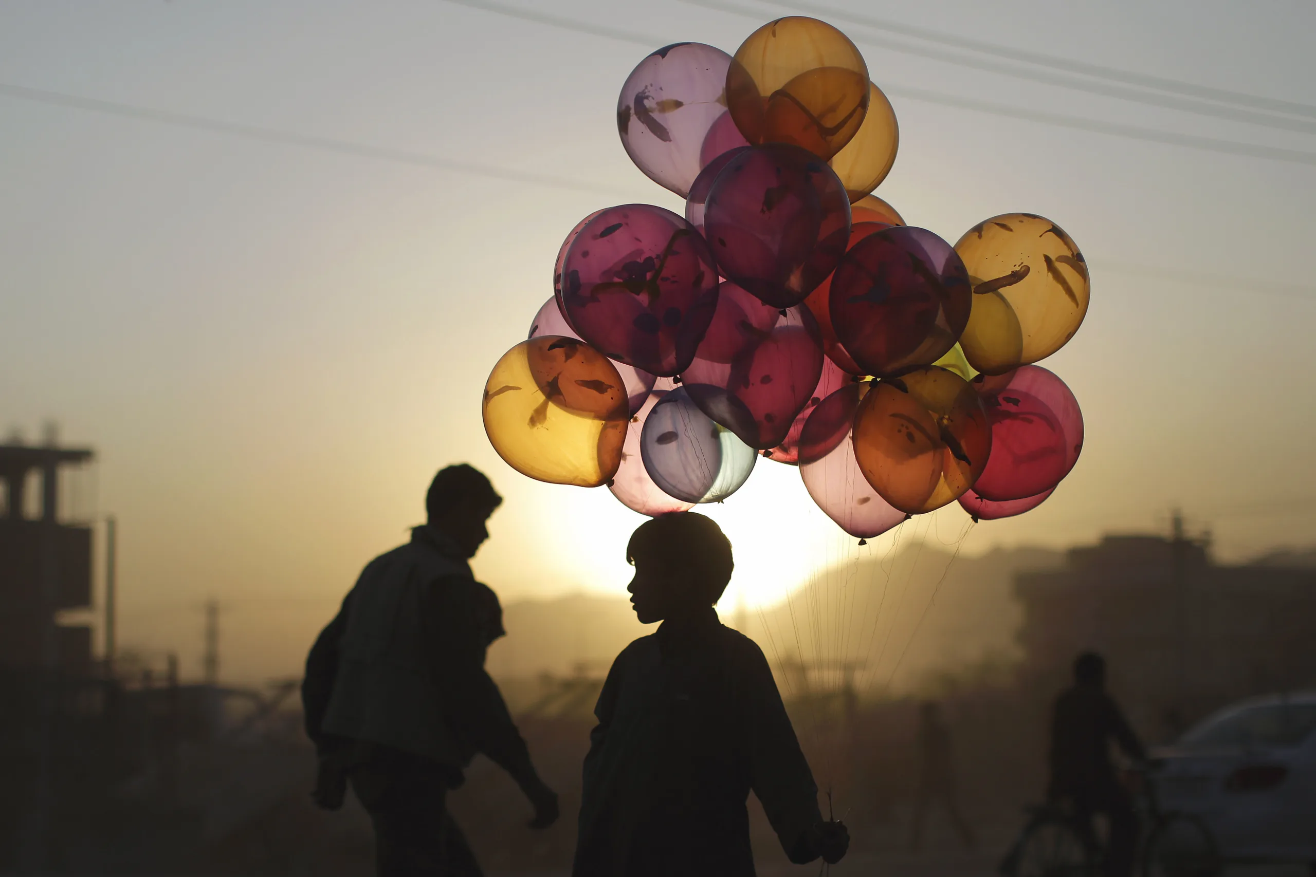 Boy holds a large collection of colorful balloons during sunset.