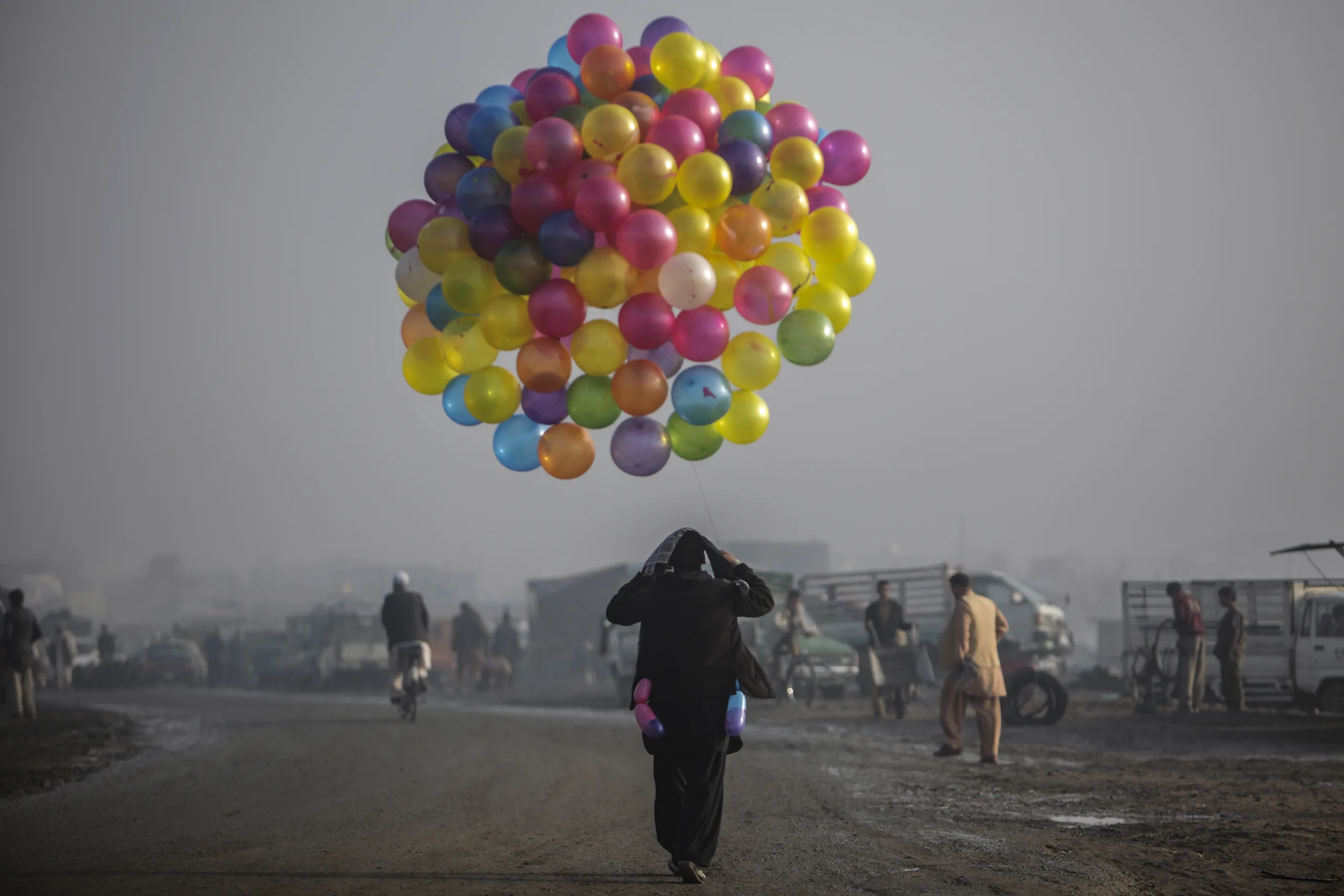 Person holds a large collection of colorful balloons as they walk down street.