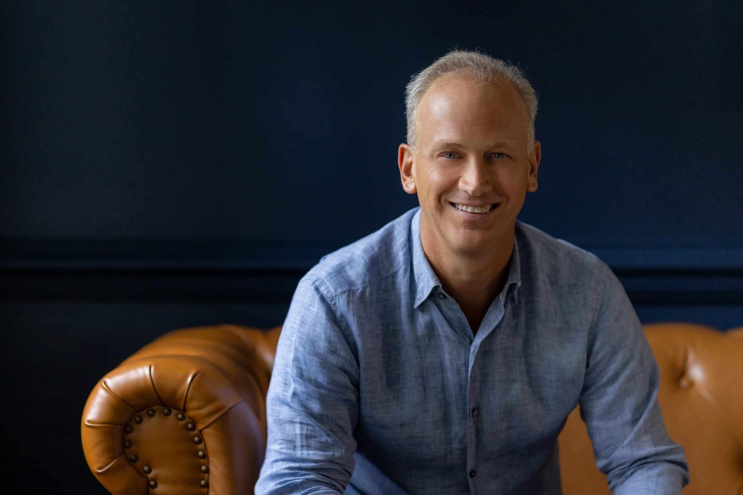 Carlos Miguel Prieto headshot wearing blue shirt on tan couch.