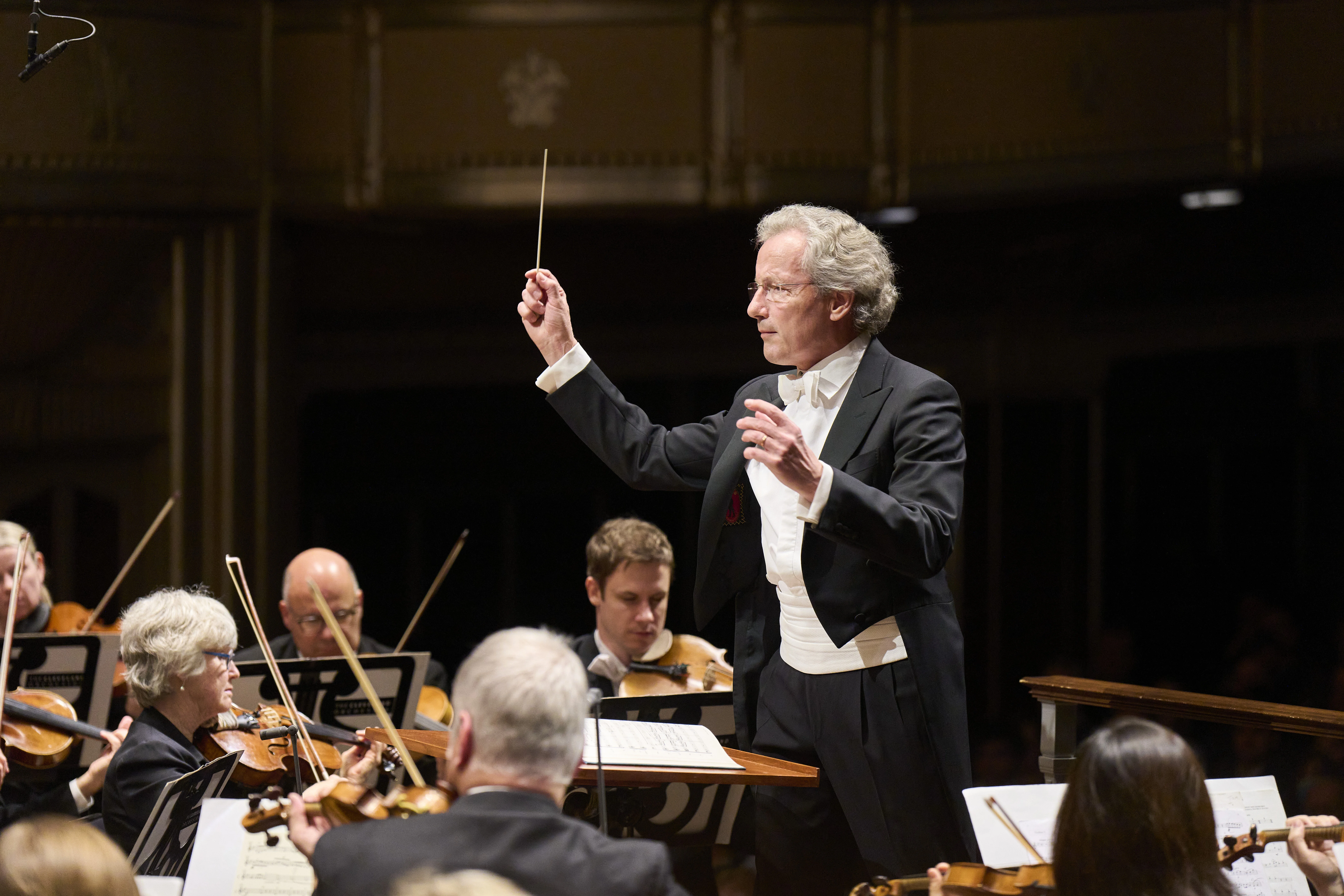 Franz Welser-Möst conducting orchestra with batton.