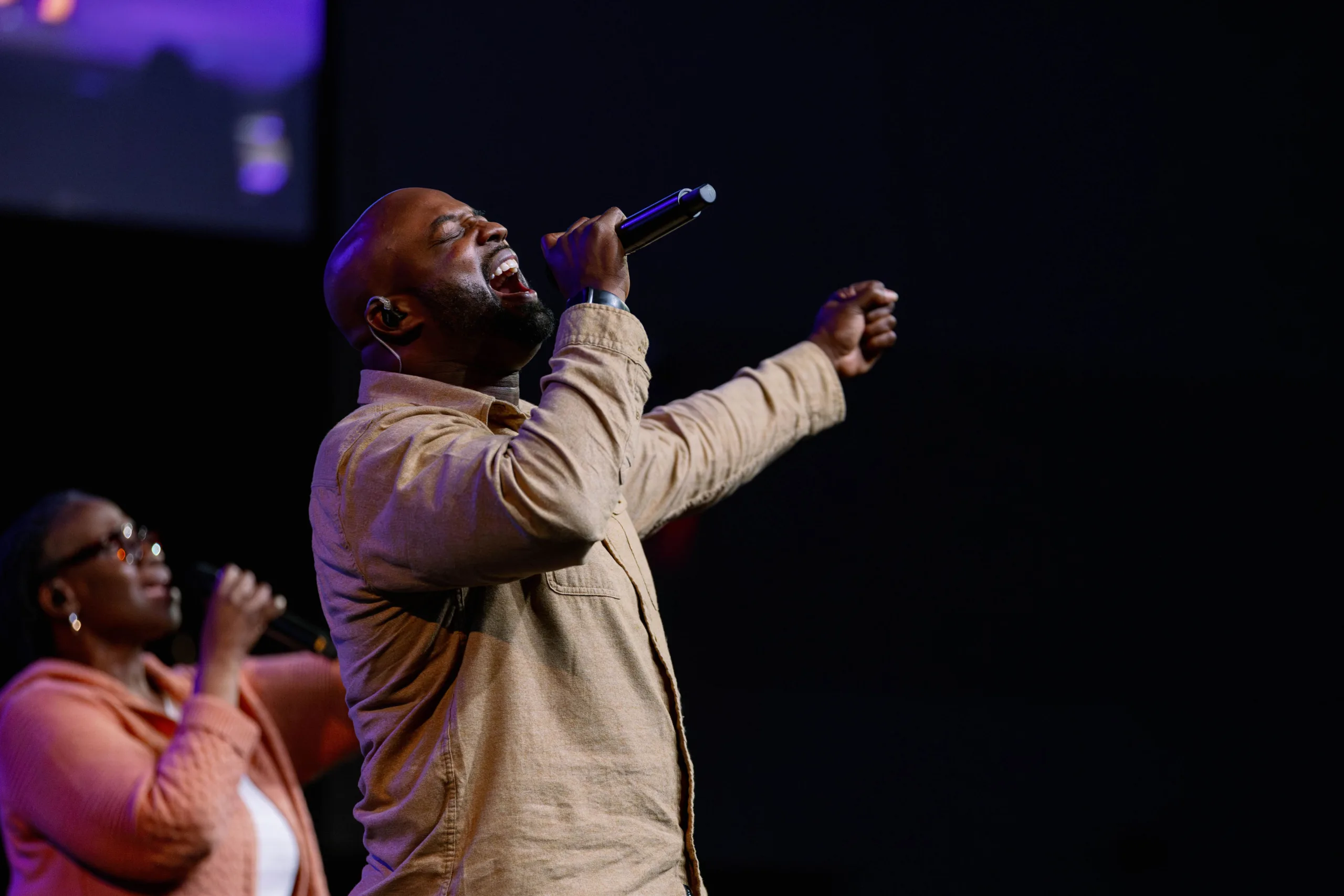 man singing on stage, women sings in background