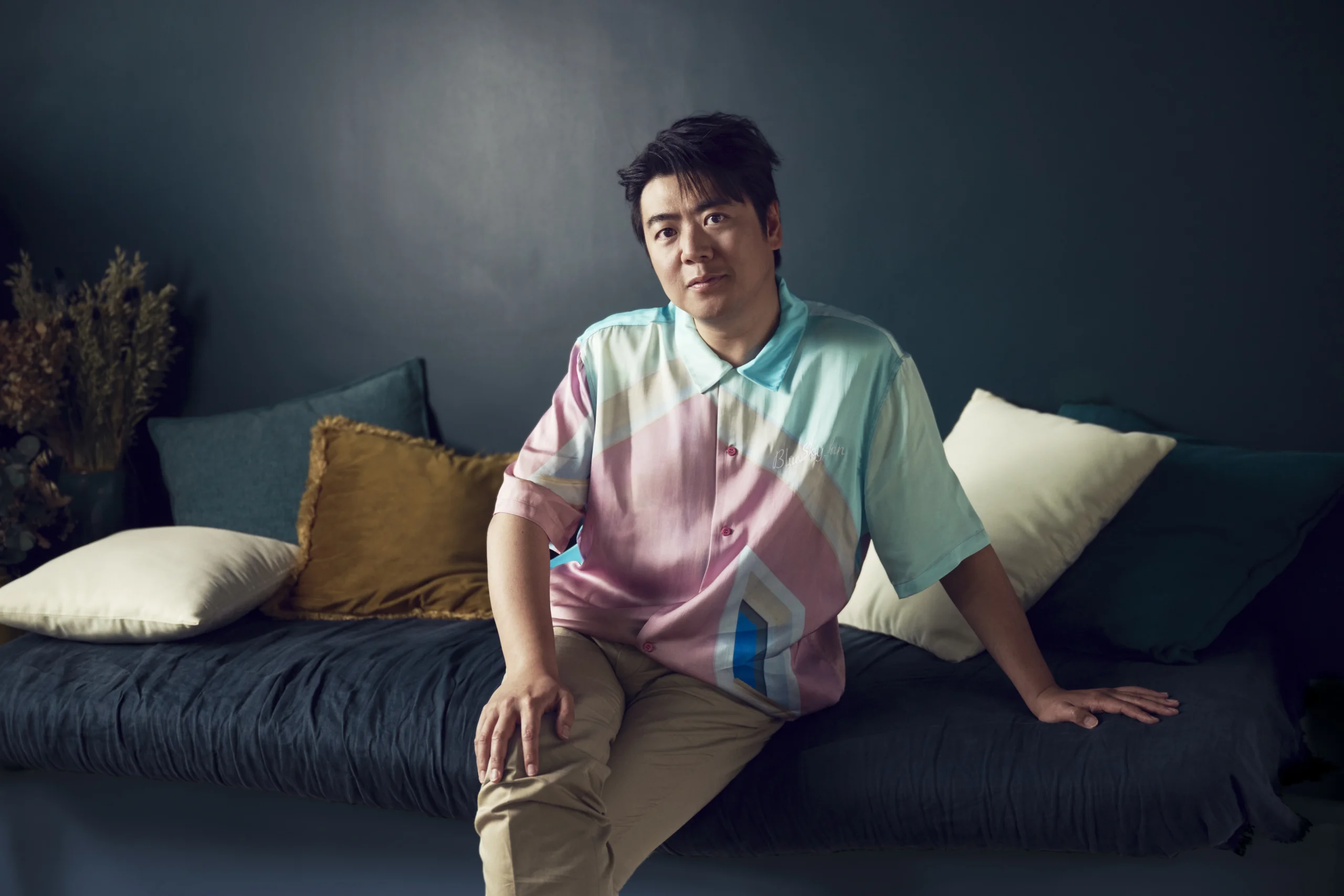 Lang Lang wearing colorful pastel shirt sitting on couch with pillows