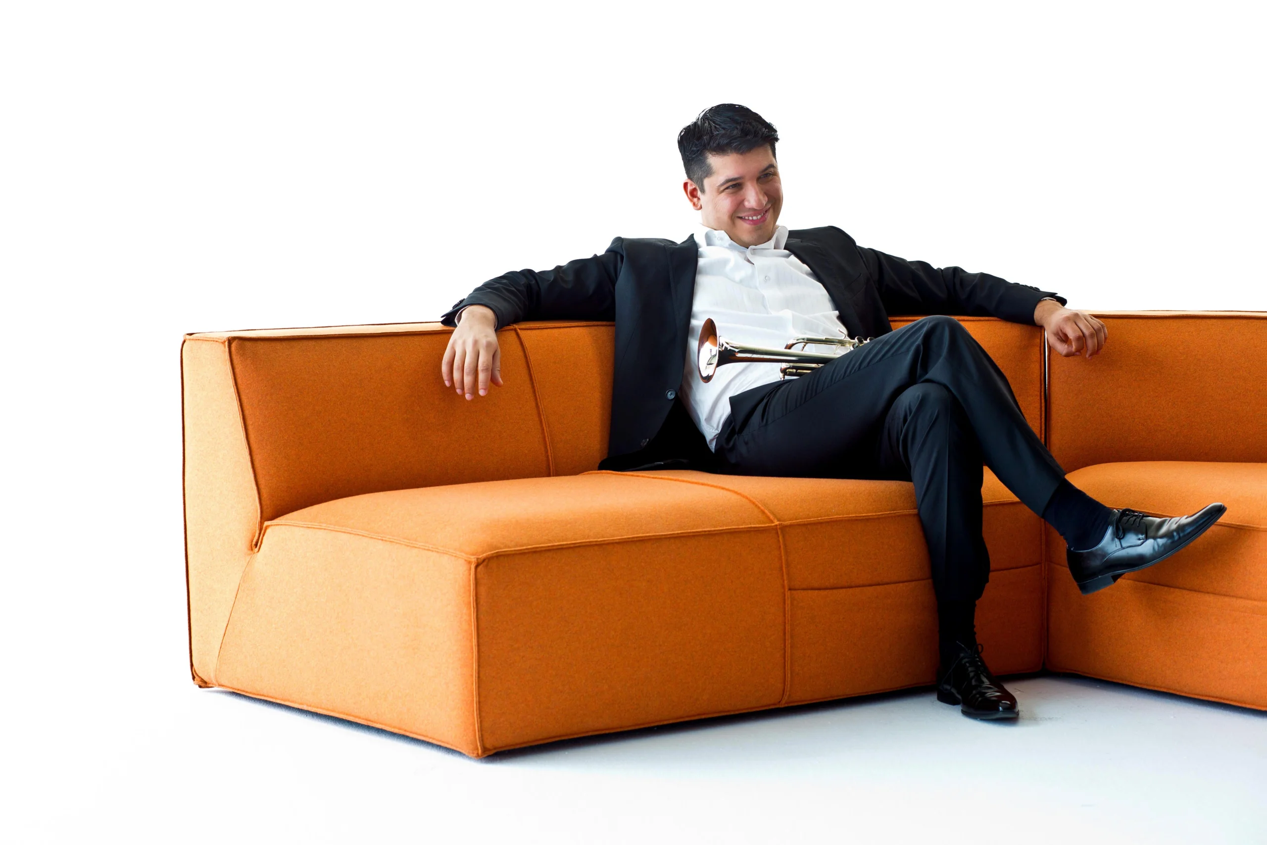 Pacho Flores sitting on a orange couch and while wearing tux, is in a relaxed pose.