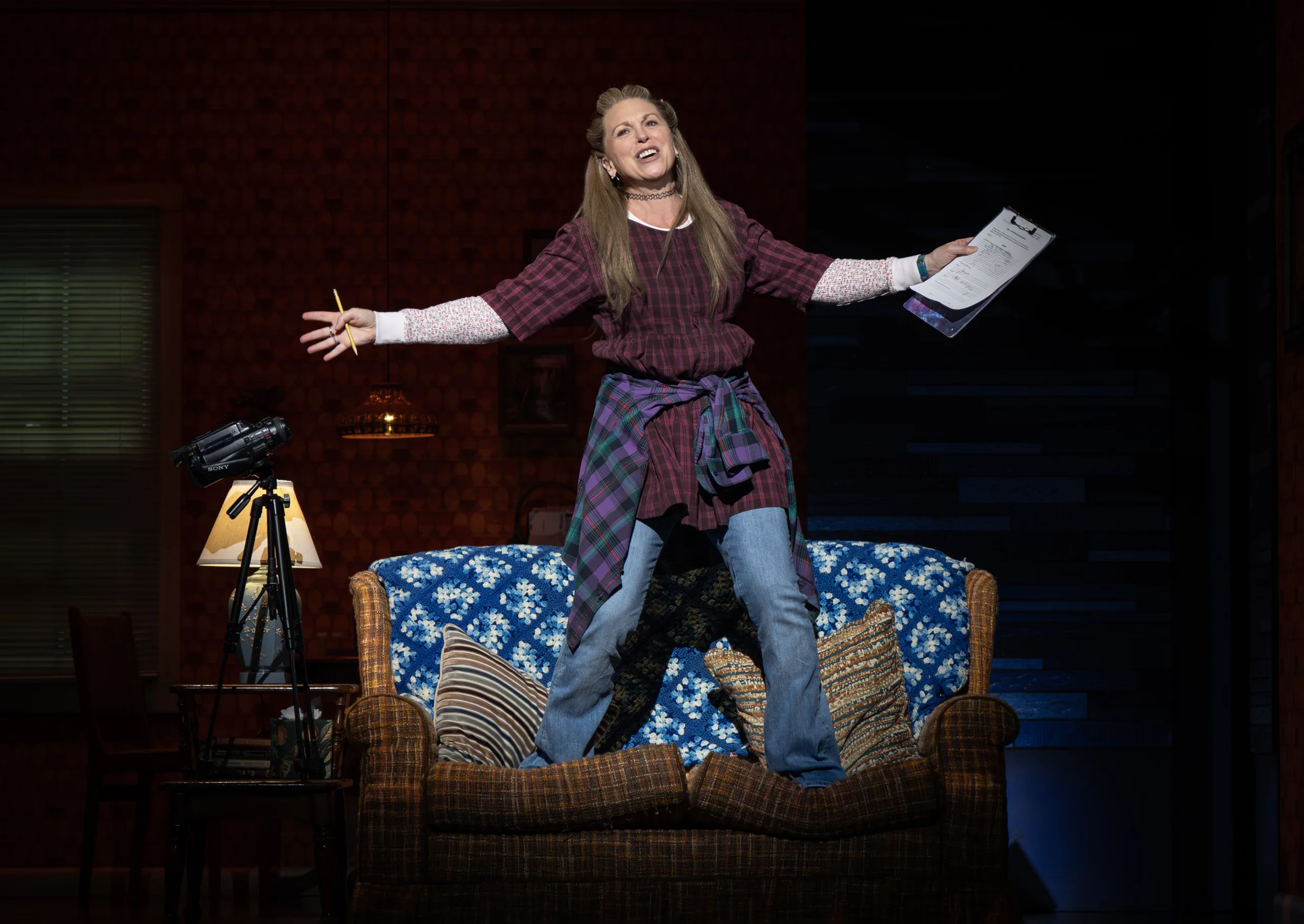 Woman standing on a couch with a spotlight on her with her arms outstretched. 