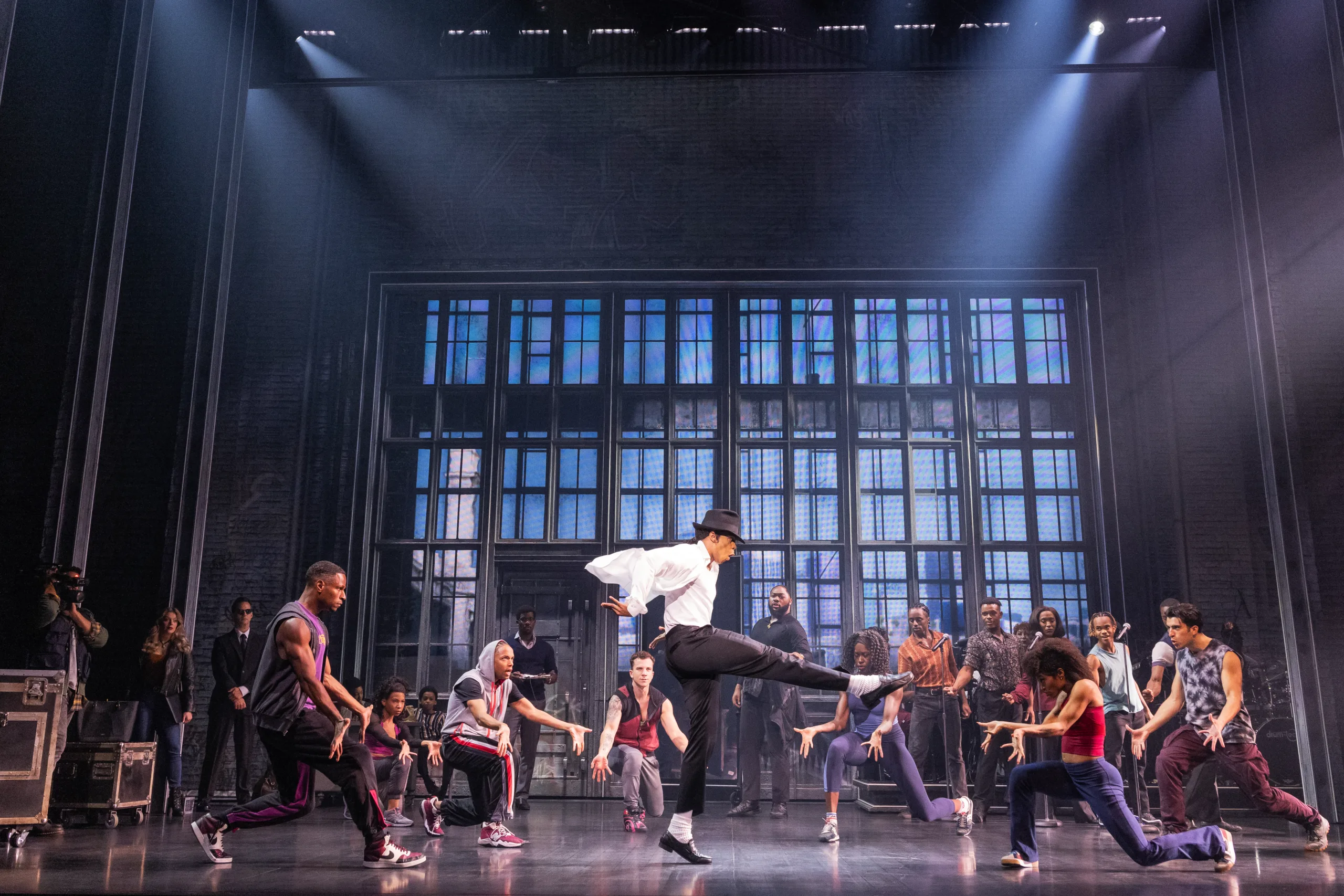 MJ in the middle showing off a dance pose while the company looks on. 