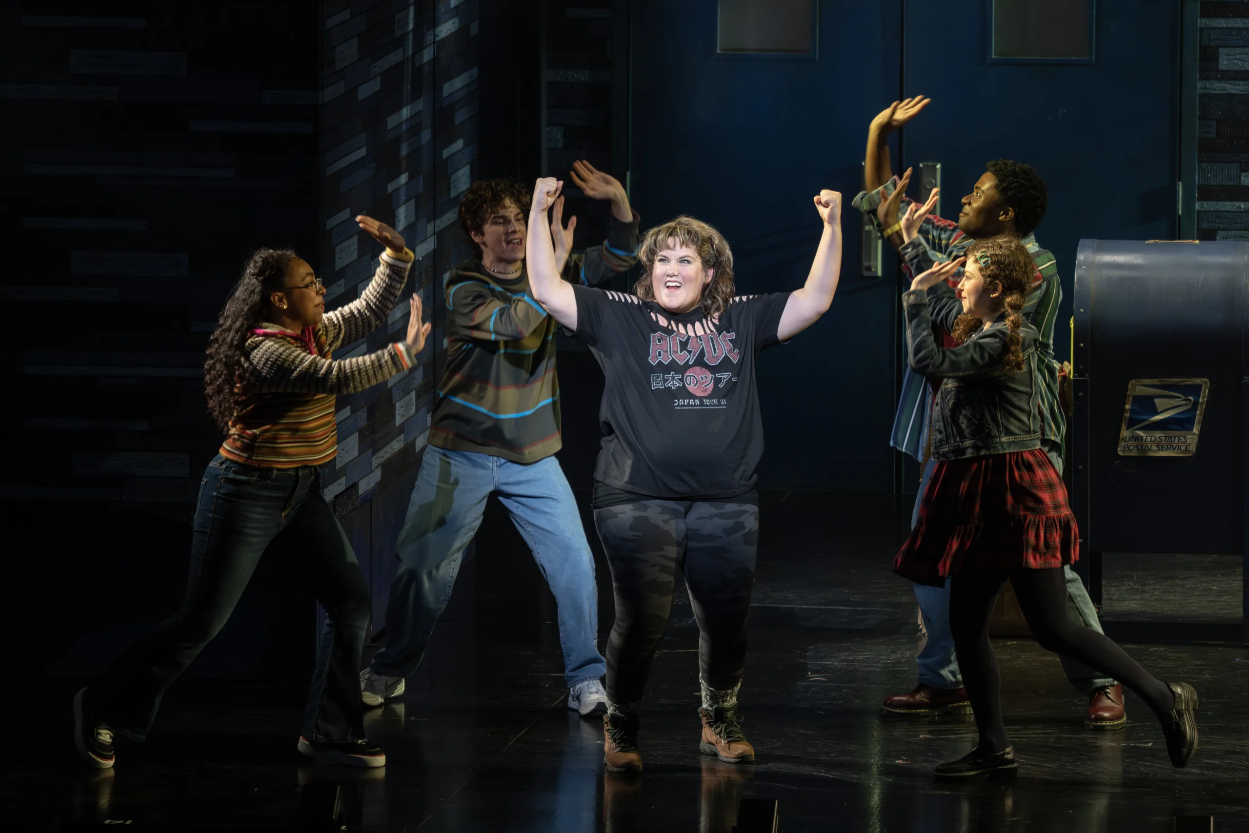 Kimberly in an ACDC shirt showing off her arms while she is surrounded by friends reaching arms out toward her. 