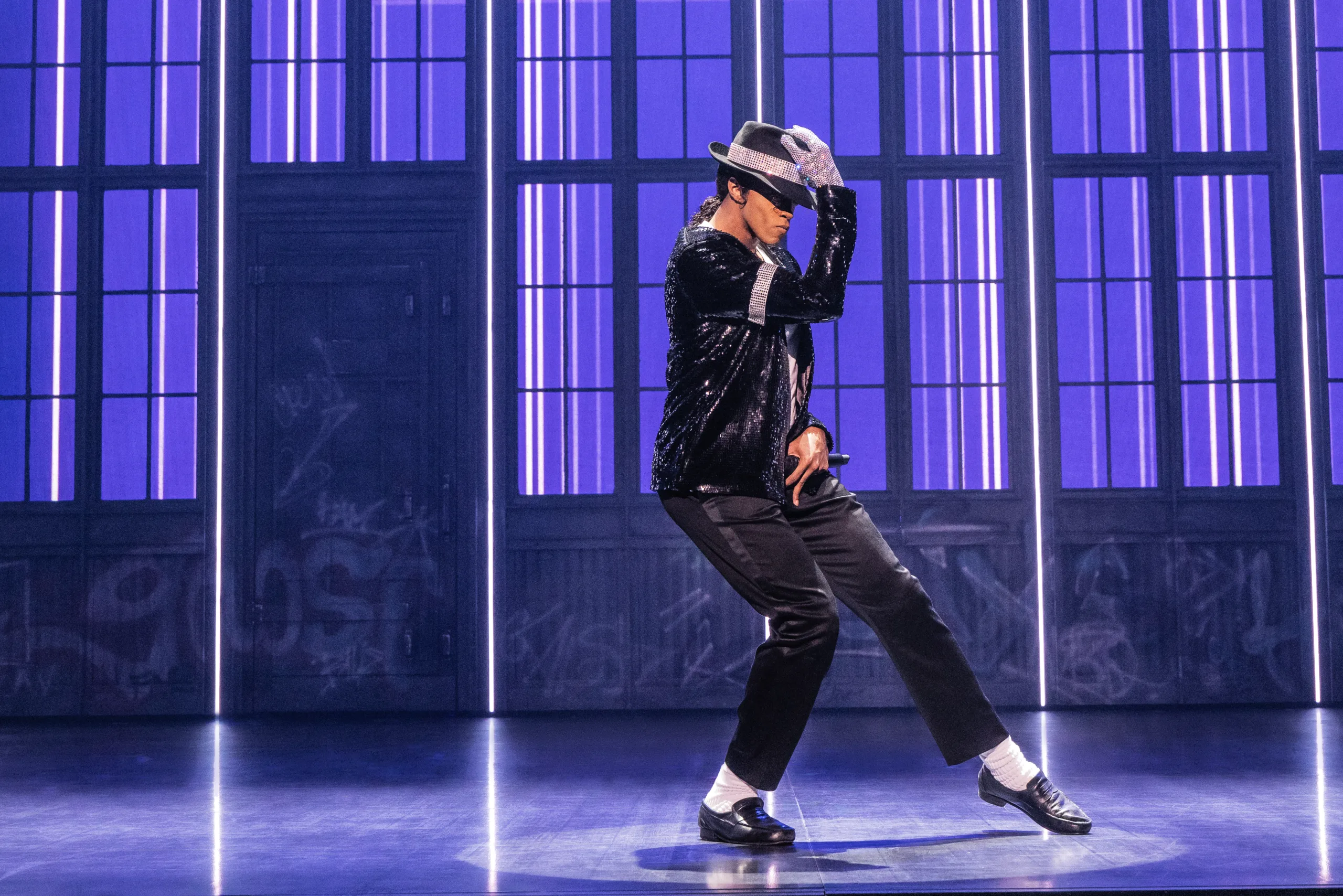 MJ wearing a black suit and fedora striking a classic MJ pose with hand on his hat. 