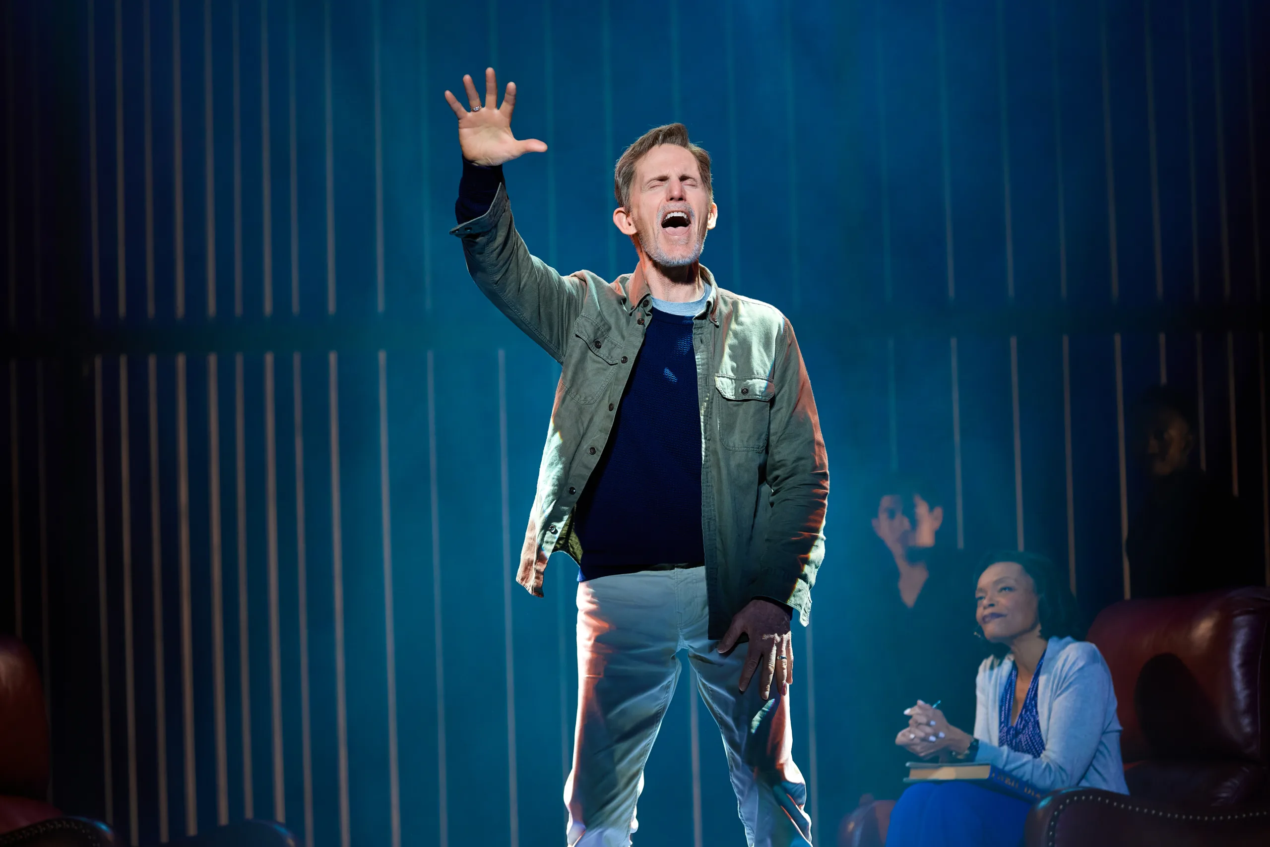 Older Neil center stage singing with his arm held out high. 