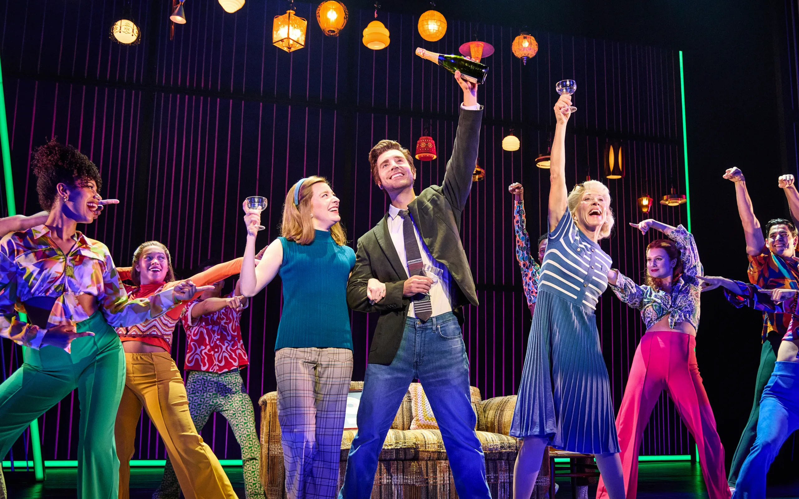 Neil holding a bottle of champagne in the air while he and everyone else toasts with their glasses pointing toward him. 