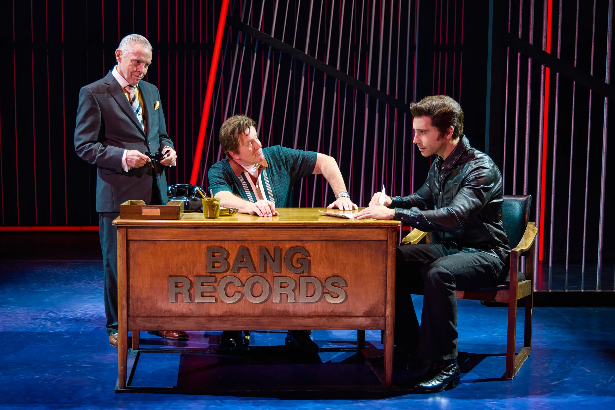 Neil signing a contract sitting at a desk at Bang Records with Tommy O'Rourke and Bert Berns.