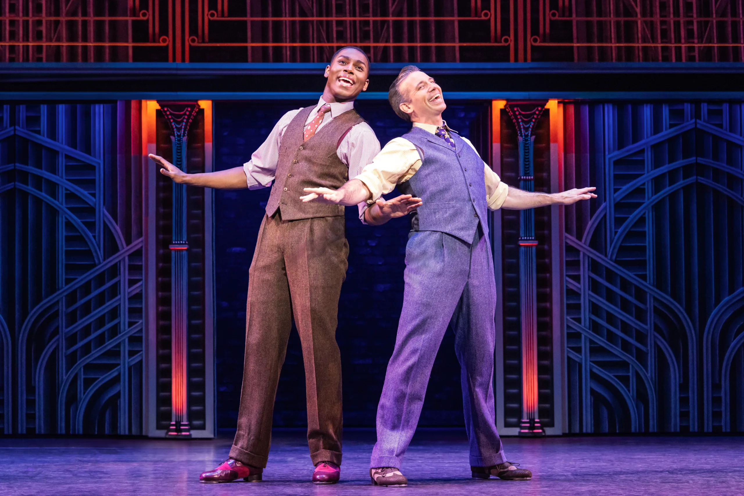 Jerry and Joe standing back to back singing with their arms outstretched. 