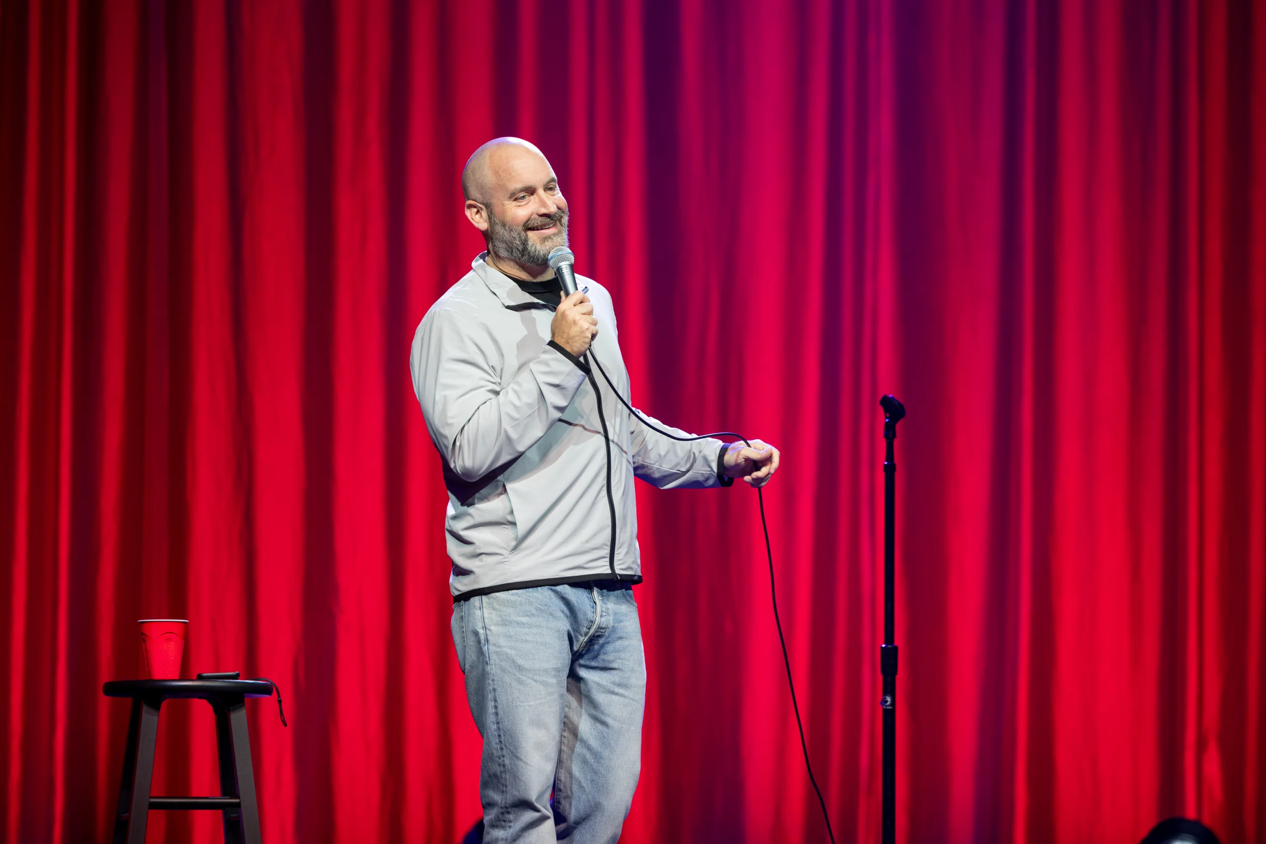 Tom Segura doing standup in front of red curtain.