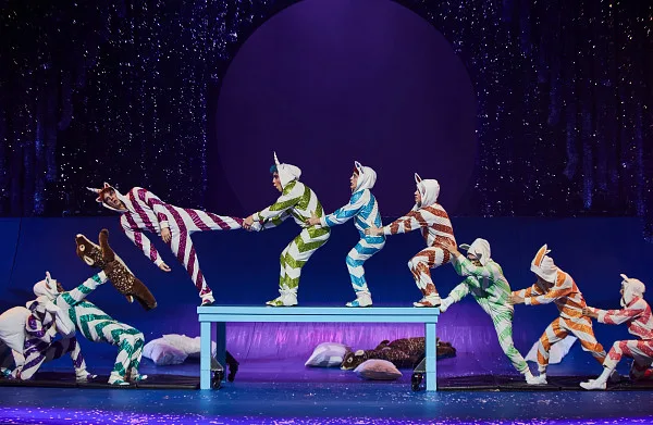 Nine performers in different candy-striped onesies as different animals holding each other by the hips. 