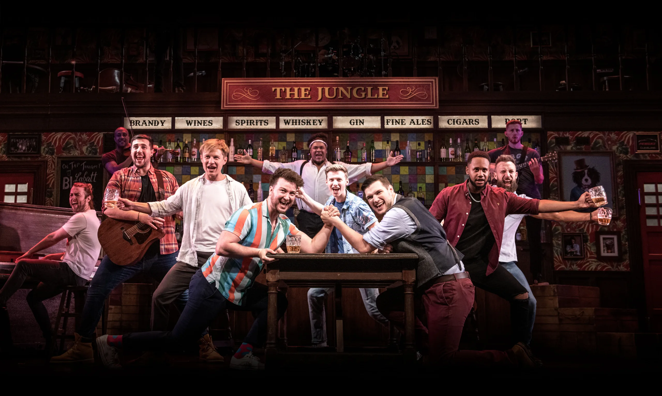 The choir surrounding two men arm wrestling across a table. 