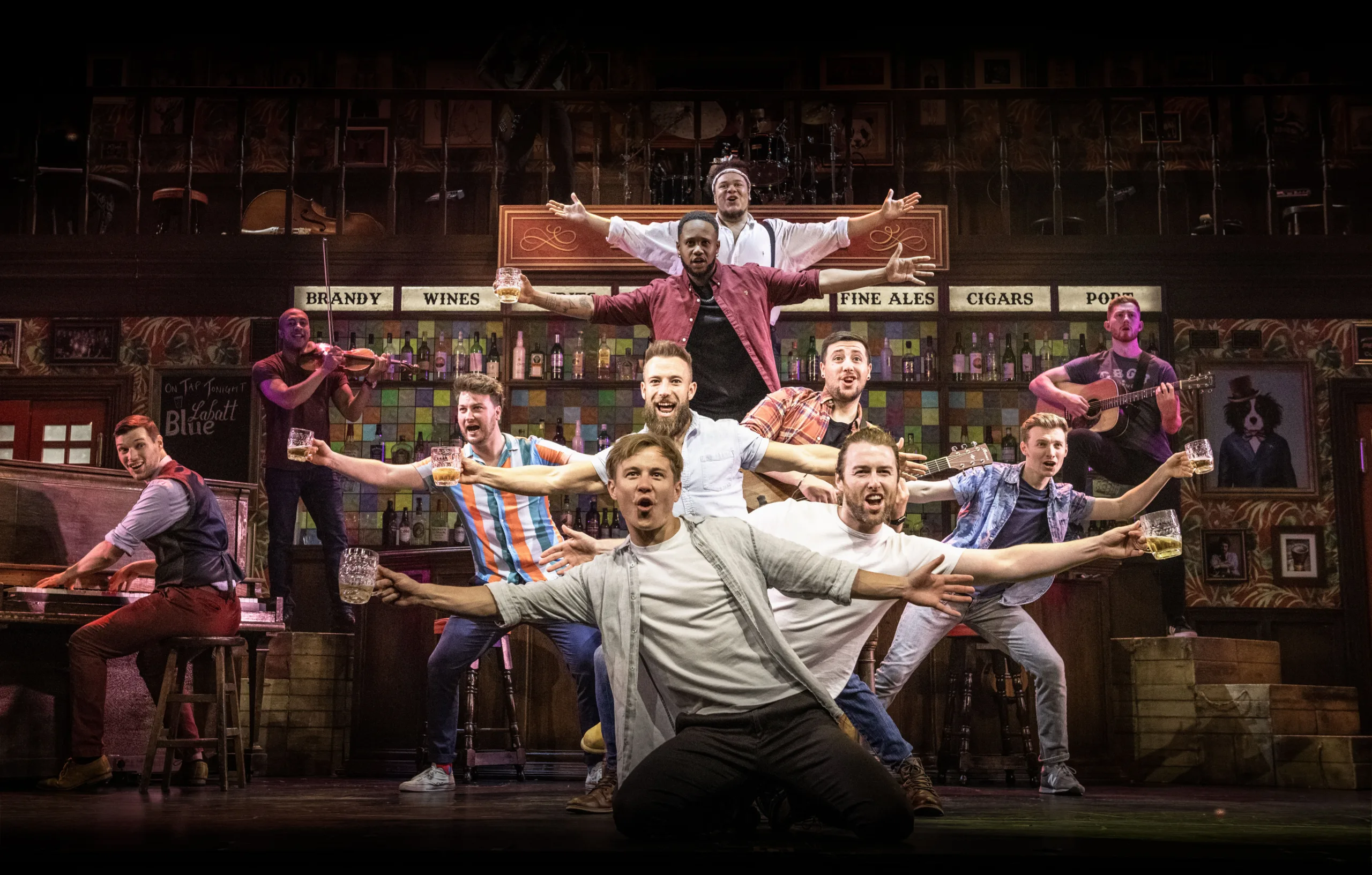 The choir of man in the pub posing with alternating arms stretched to the left and right. 