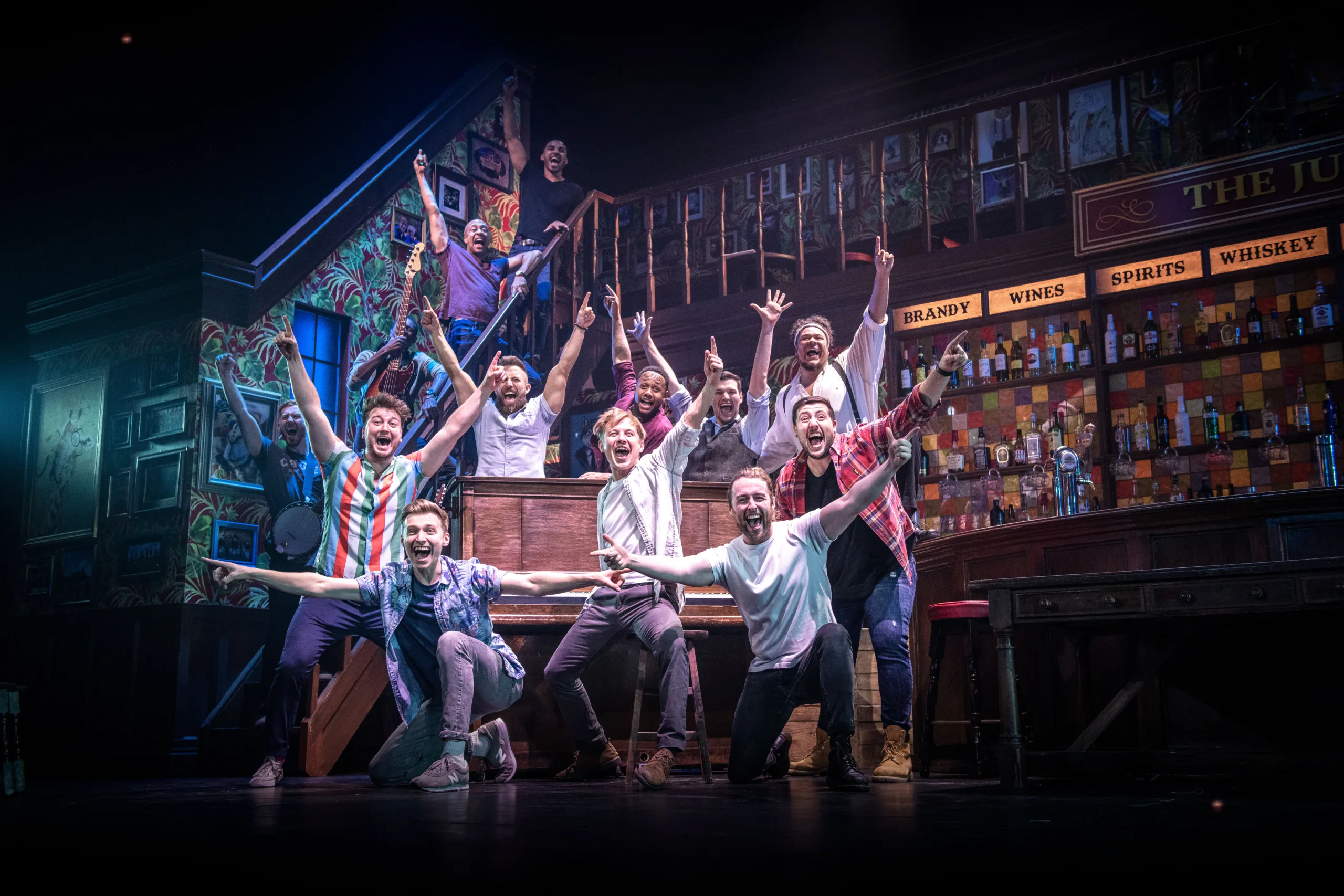 The choir of man in the pub posing with a piano with arms stretched out.
