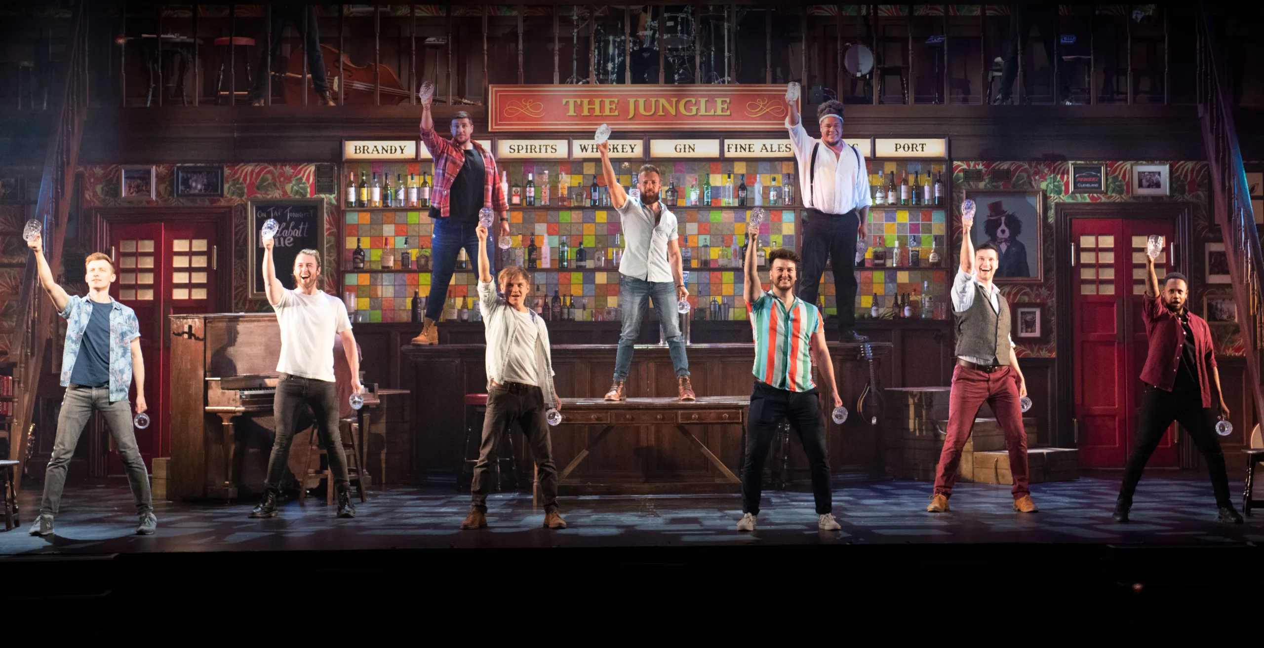 6 members of the choir of man on stage raising their glasses high.