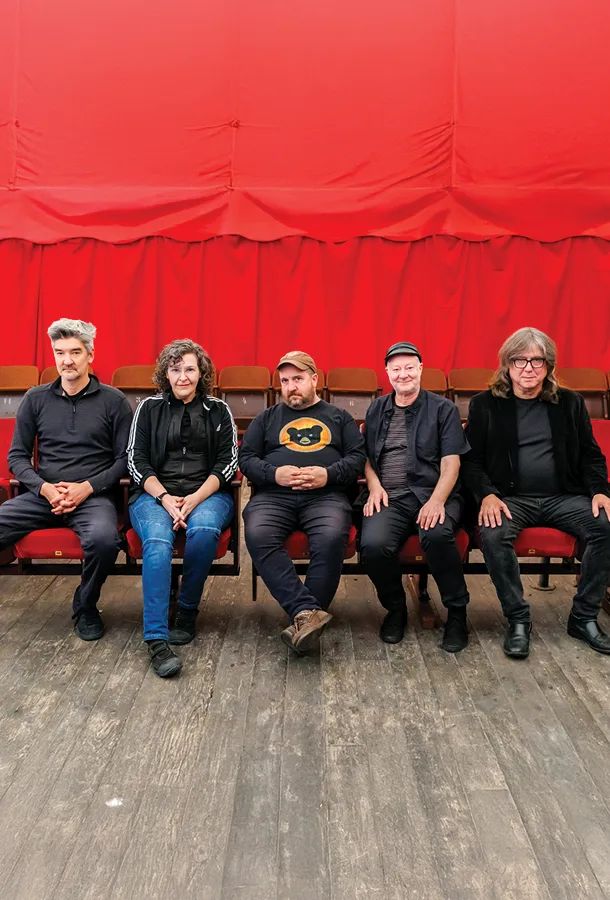 The five members of Magnetic Fields wearing black, seated in red theatre seats looking into the camera.
