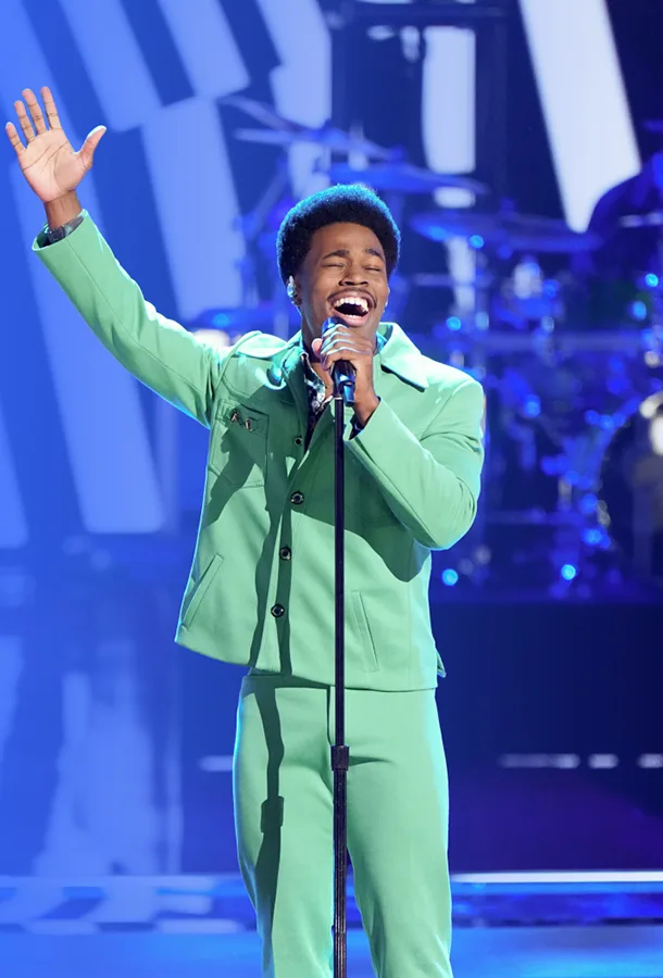 Nathan Chester on stage in a mint green suit singing into a microphone with one arm raised.