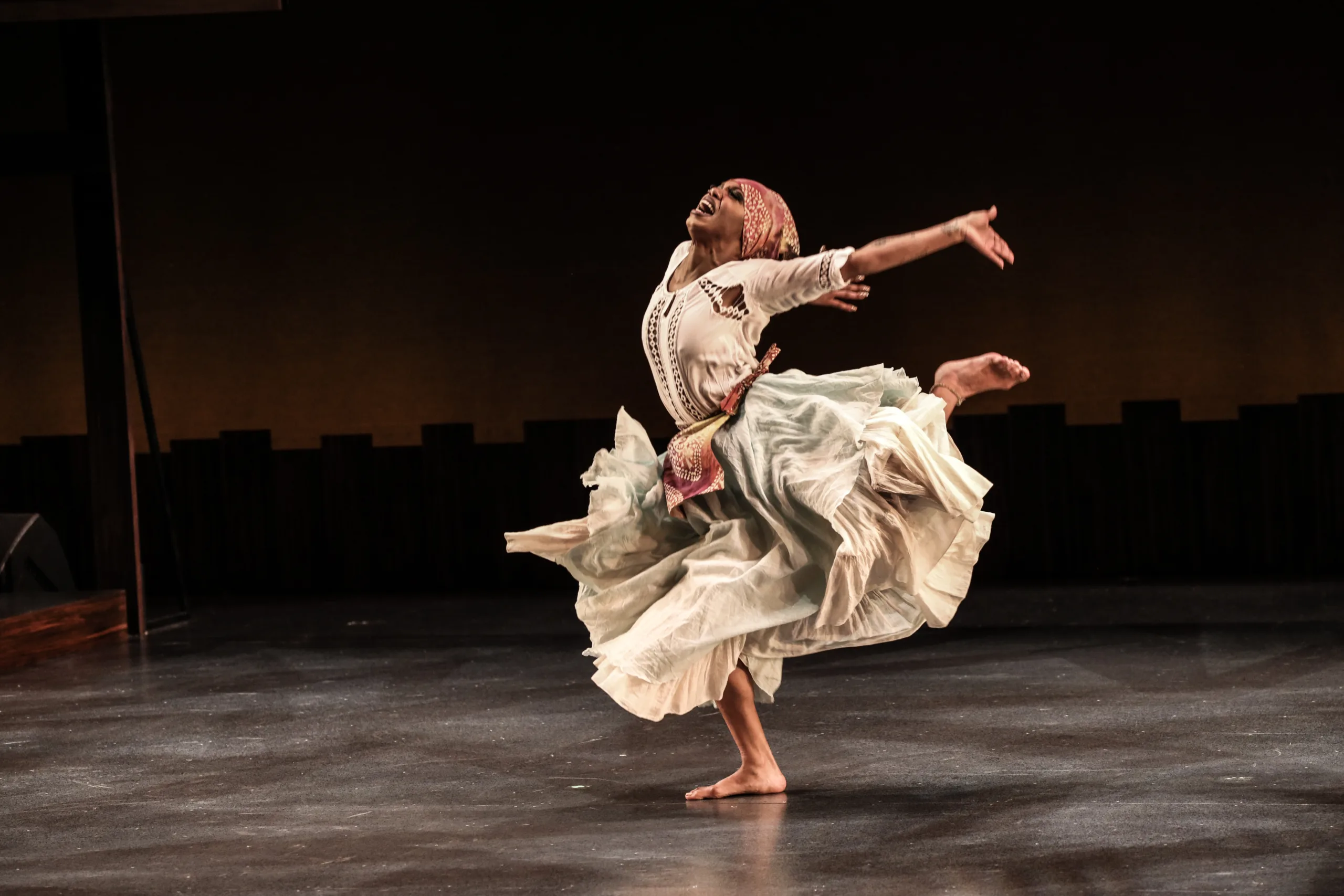 Woman flinging her head back in dancer pose with billowing white skirts flowing around her.
