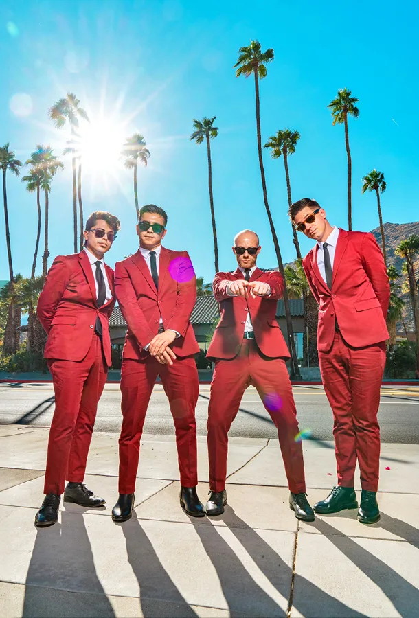 The four "Dreamboats" in bright red suits standing on pavement with bright sun and palm trees in the background.