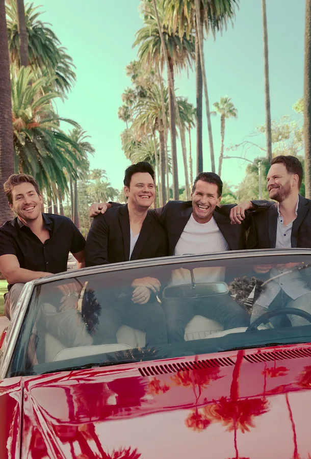 The four "Modern Gentlemen" sitting in a row in an open convertible with palm trees in the background.