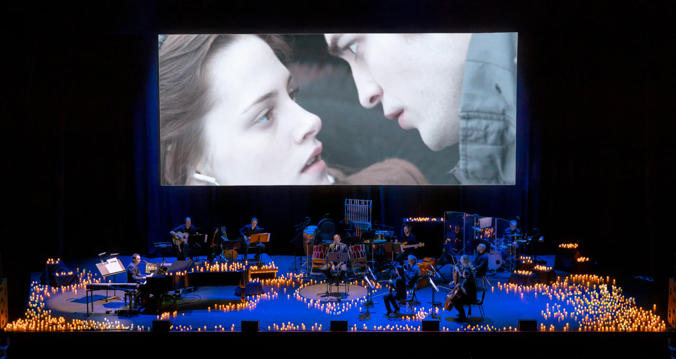 Film projection of Edward and Bella staring into each other's eyes over the stage featuring the full band and a thousand candles and blue stage lights.