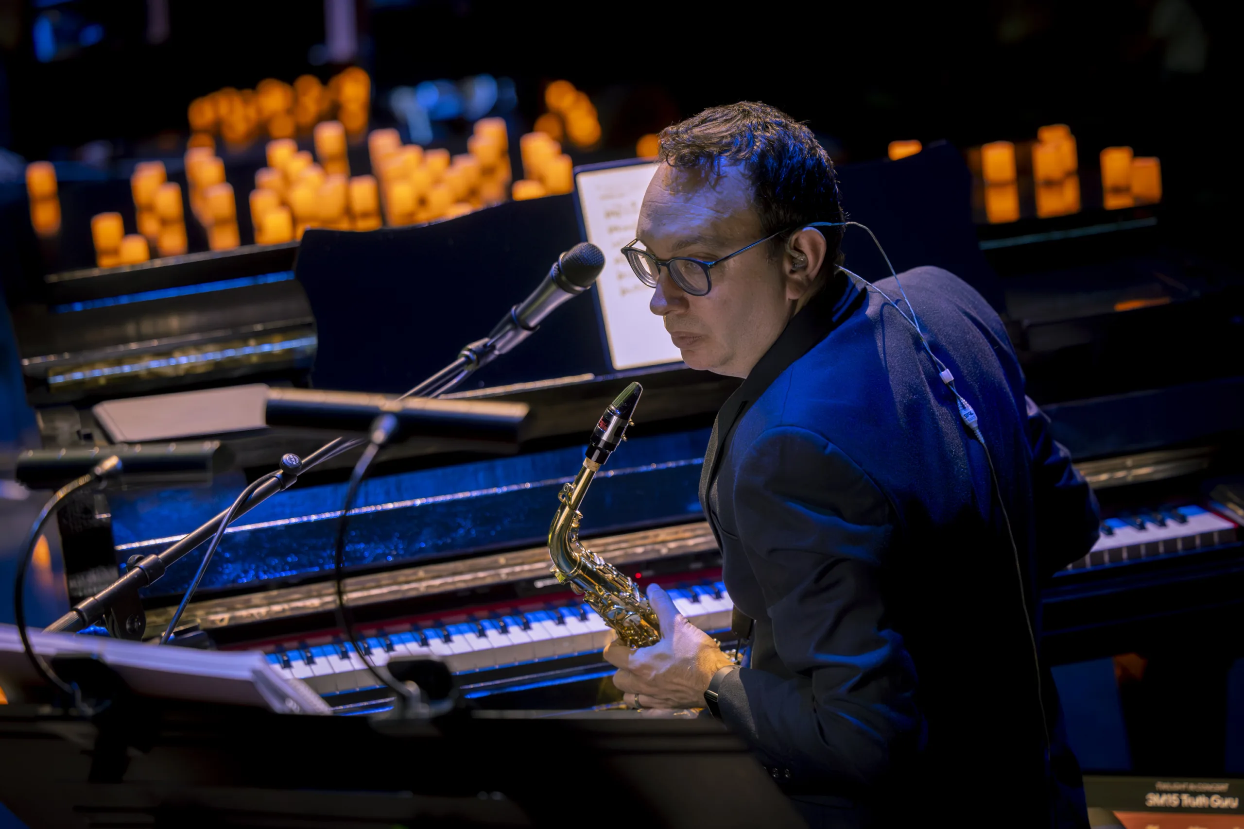Saxophone player looking over his shoulder in front of piano with lighted candles in the background.