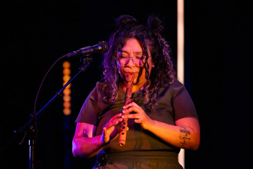 Satya Chavez performs with wooden wind instrument on stage.