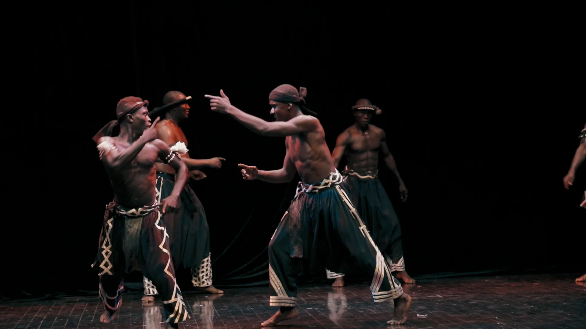 Four dancers of Les Ballets Africains on stage in costume posing.