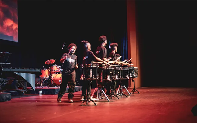 students perform with snare drums on stage.