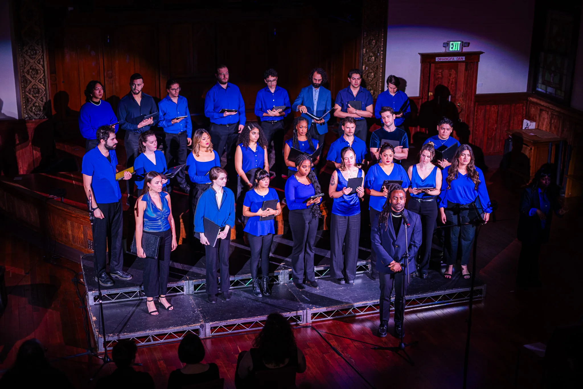 Tonality choir wearing bright blue shirts with a solo performer in the front standing at a microphone