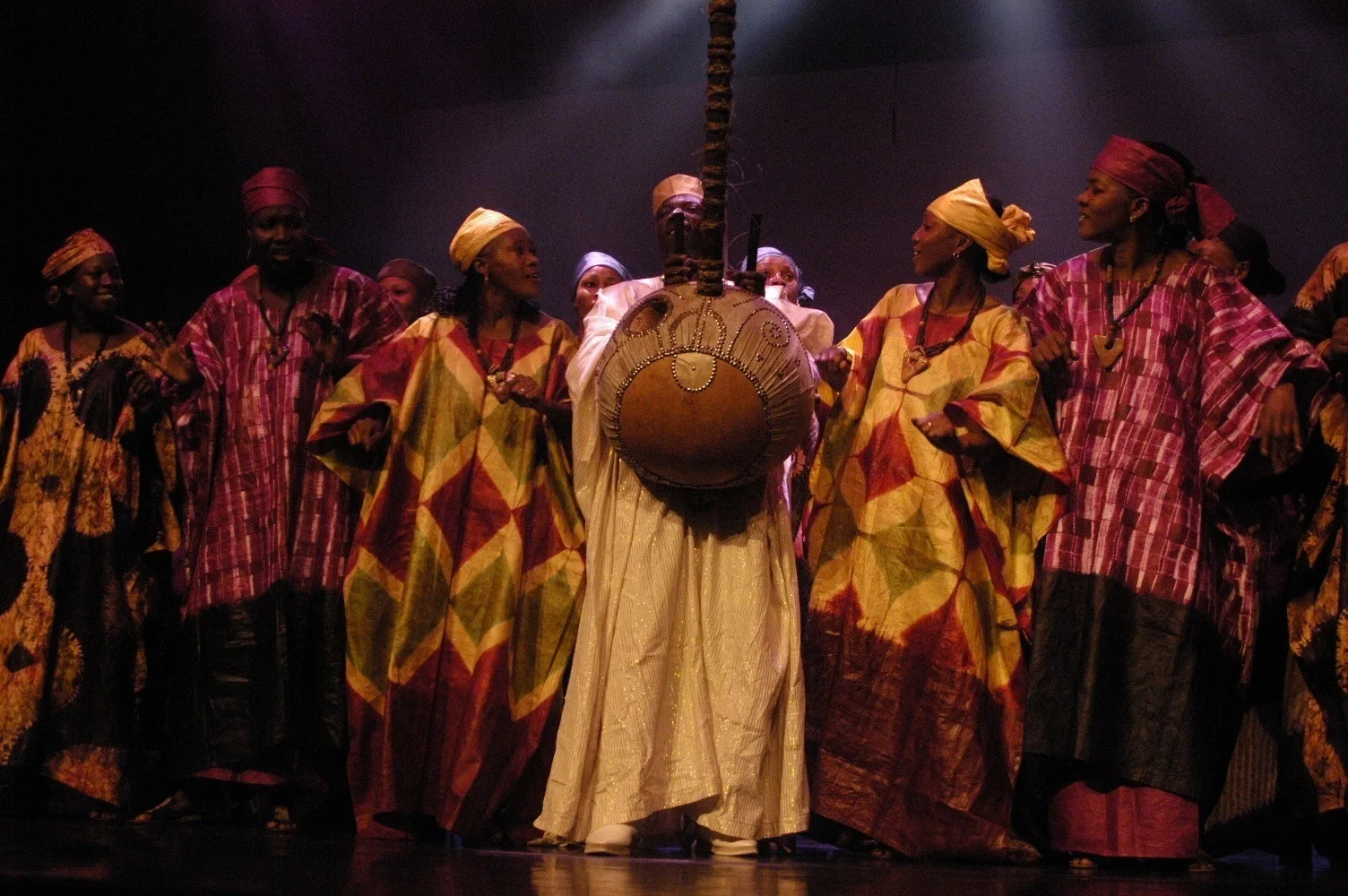 The company of Les Ballets Africains on stage in costume dancing in formation.