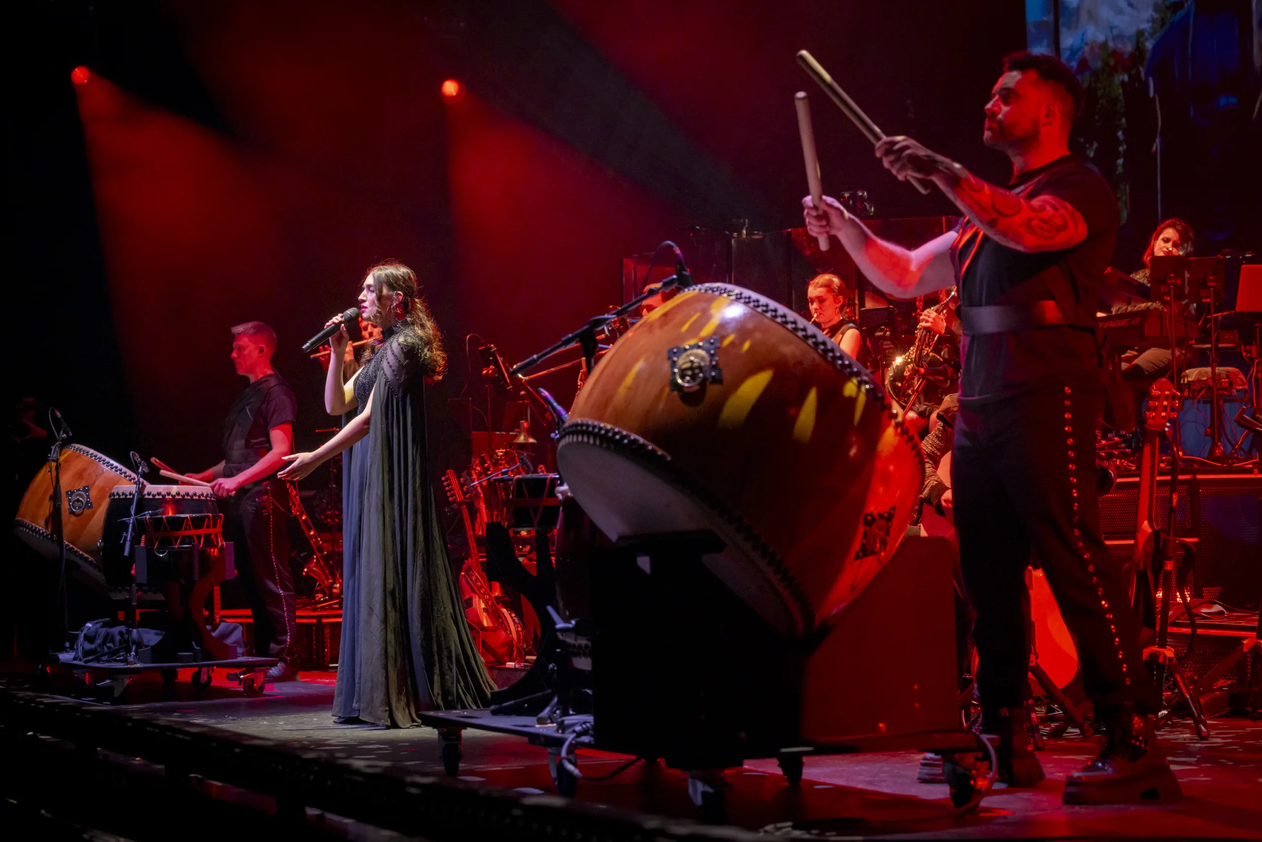 The band on stage in red lighting featuring the drummers with projections from 