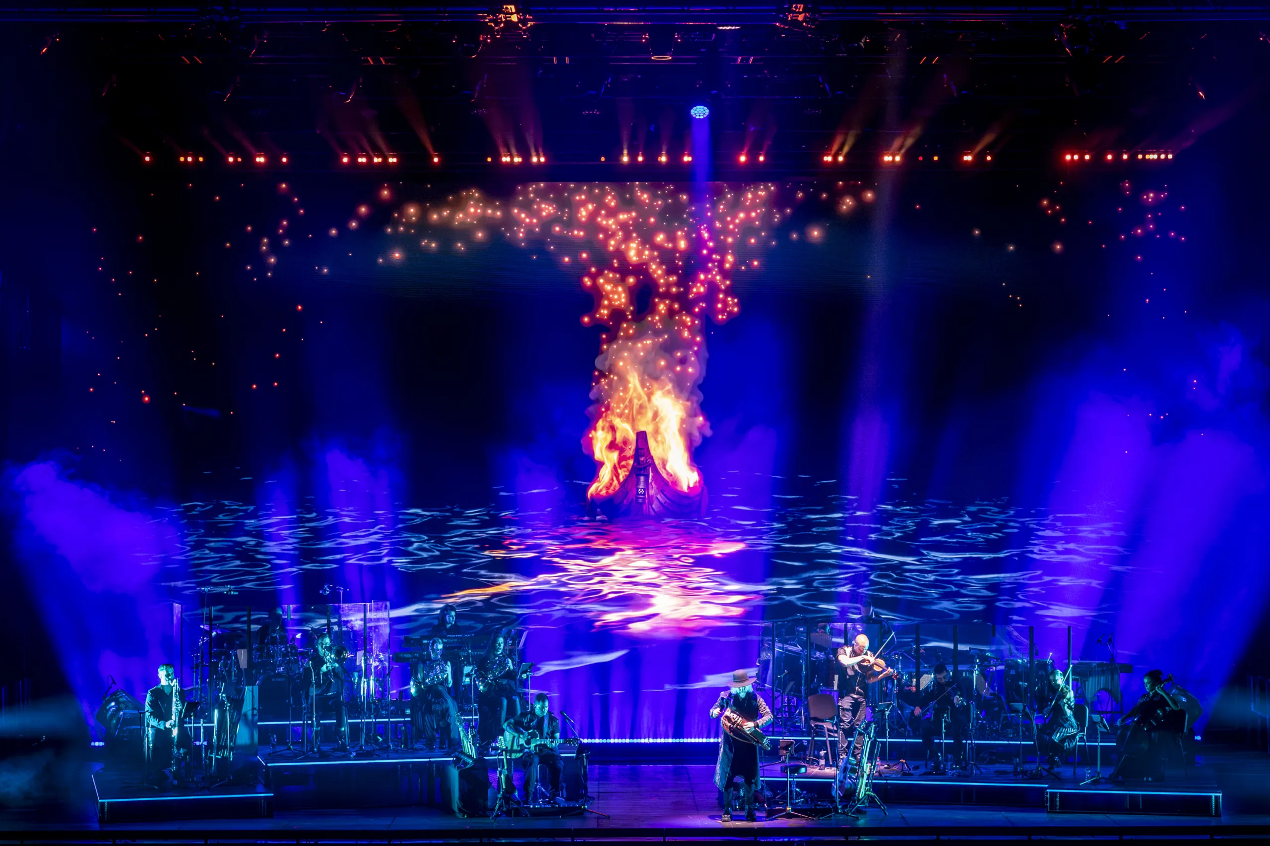 The band on stage in soft blue light surrounded by projections from 