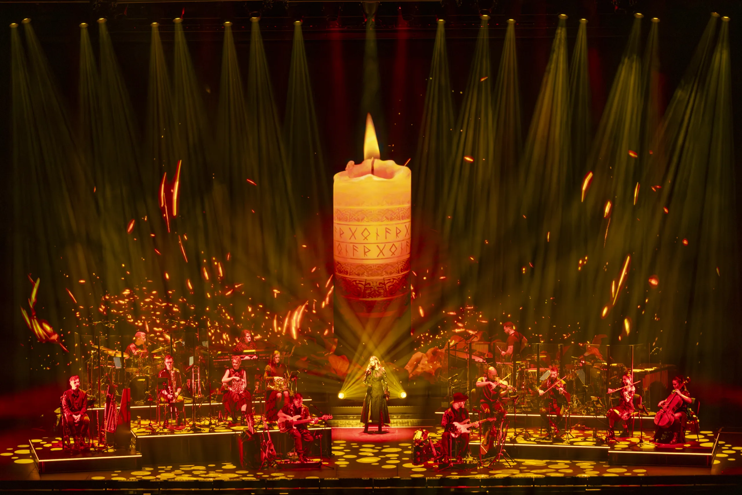 The band on stage in fiery orange light surrounded by a giant candle projection from 