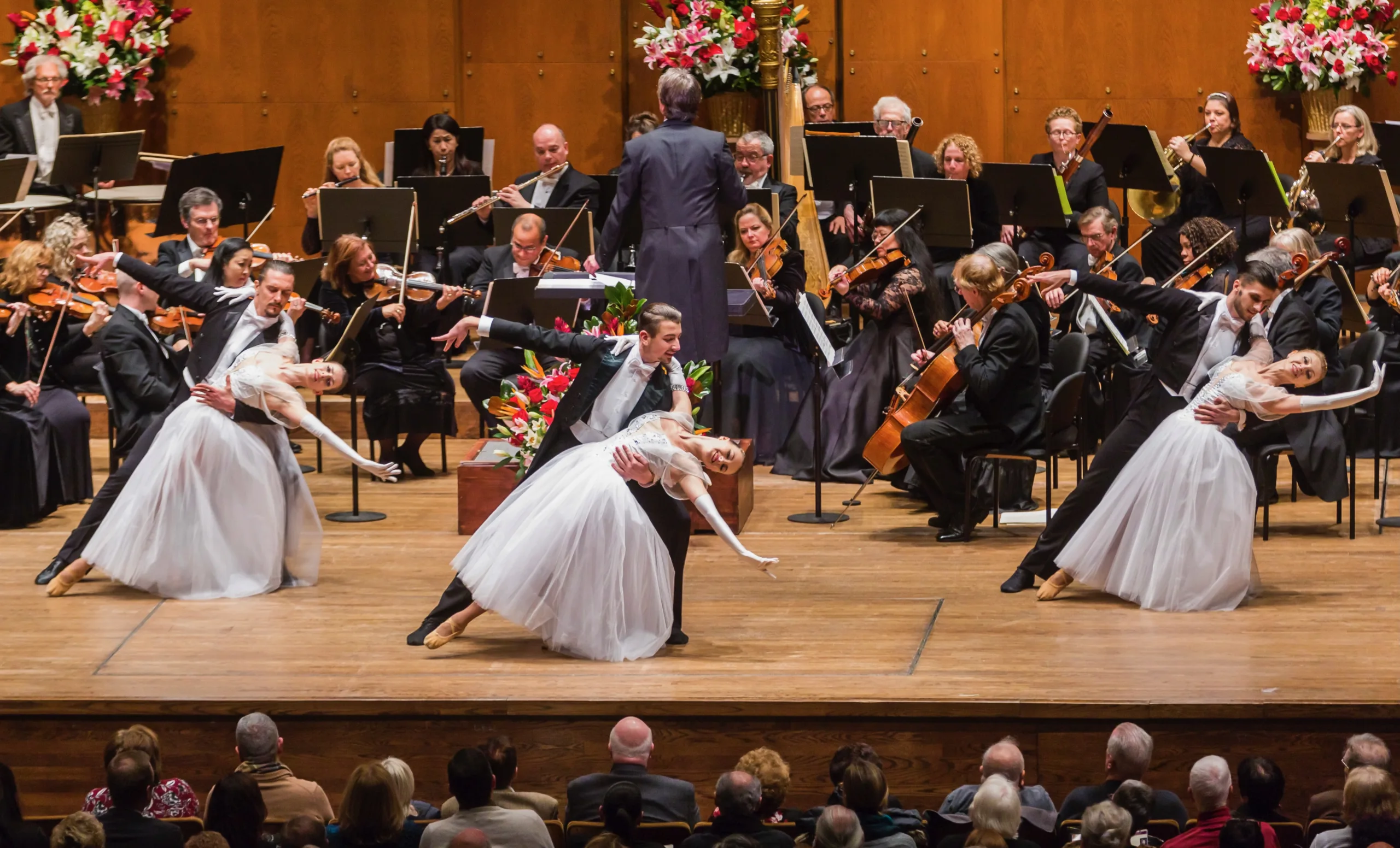 Salute To Vienna ballroom dancers in white gowns being dipped by the male dancerswith the orchestra around them on stage.