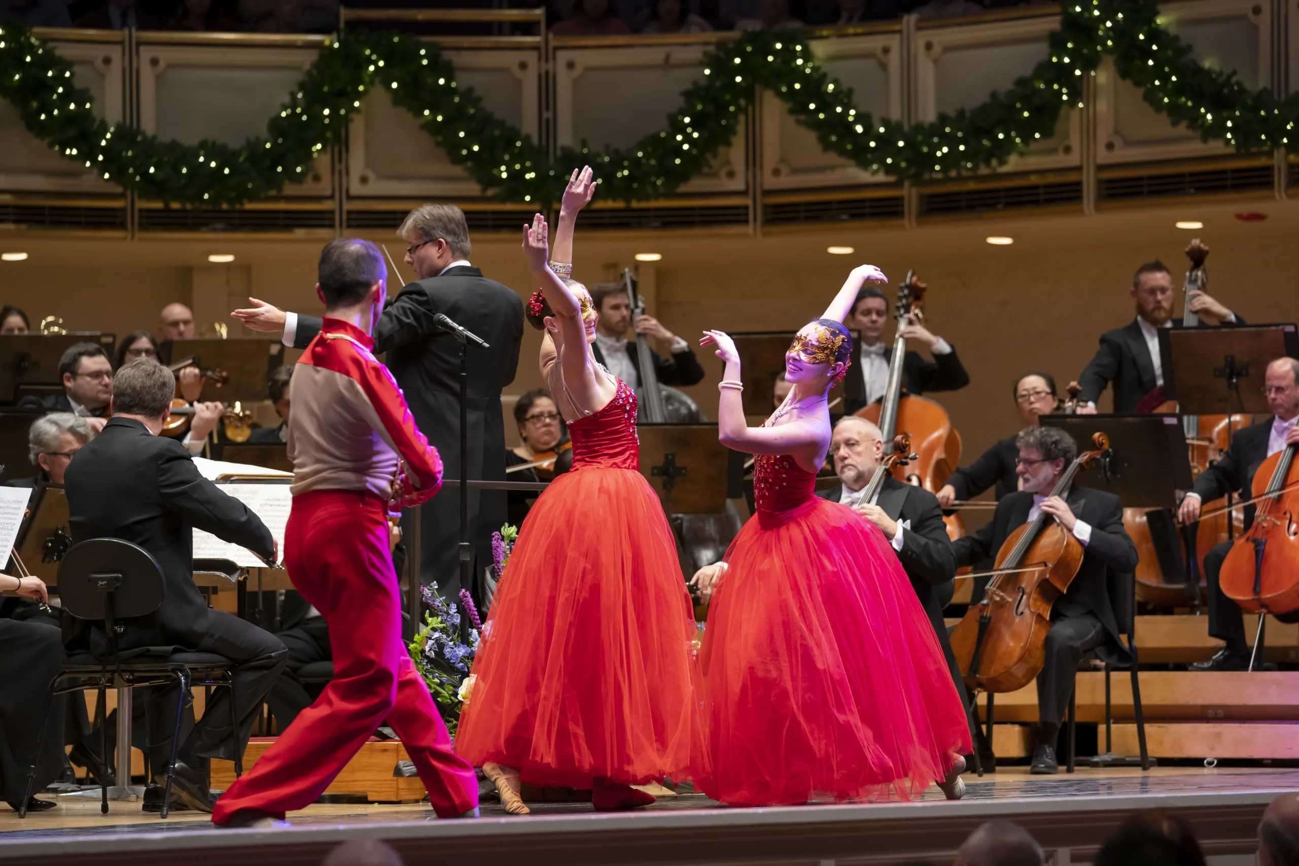Salute To Vienna ballroom dancers in red gowns posing with the orchestra around them on stage.