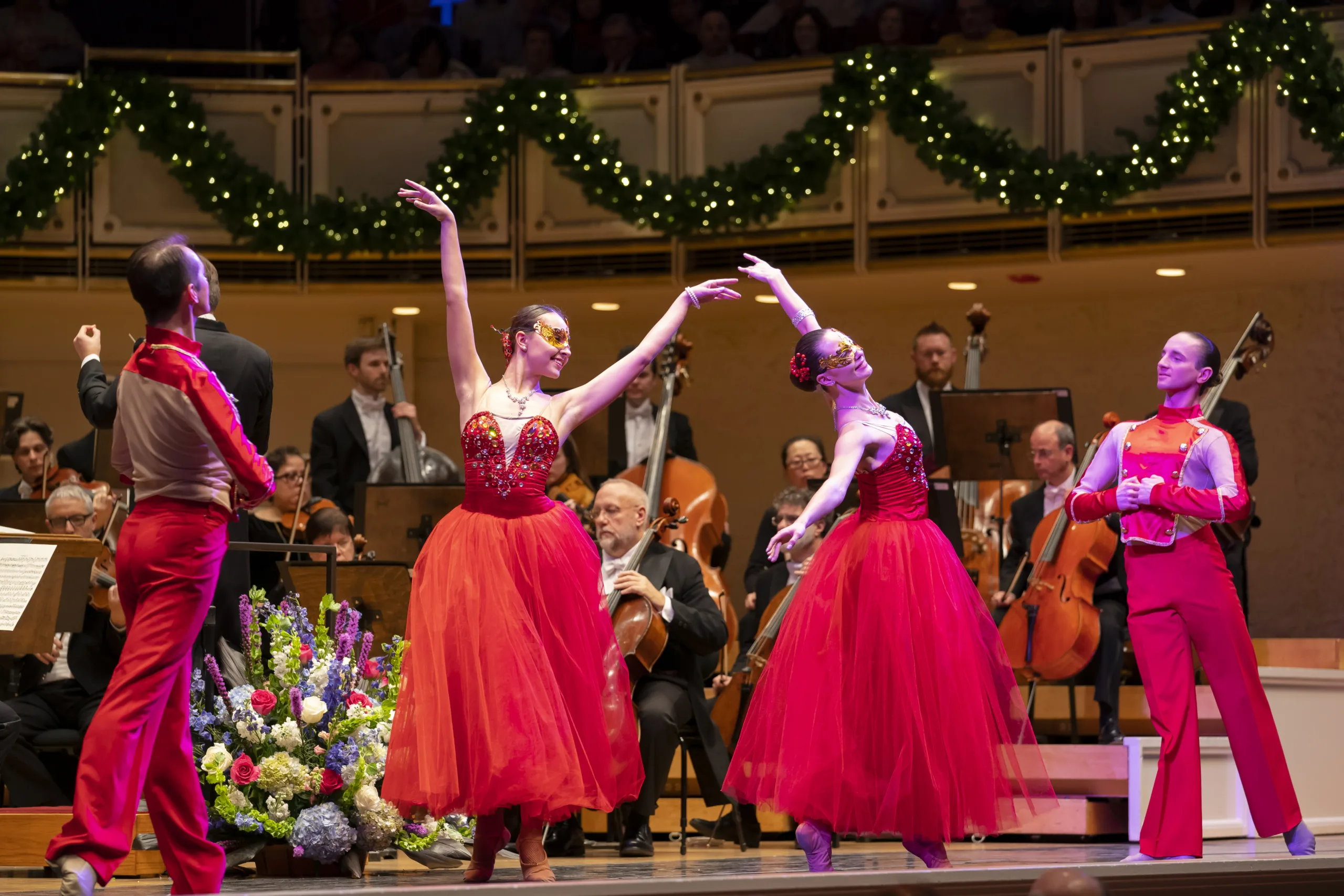 Salute To Vienna ballroom dancers in red gowns posing with the orchestra around them on stage.